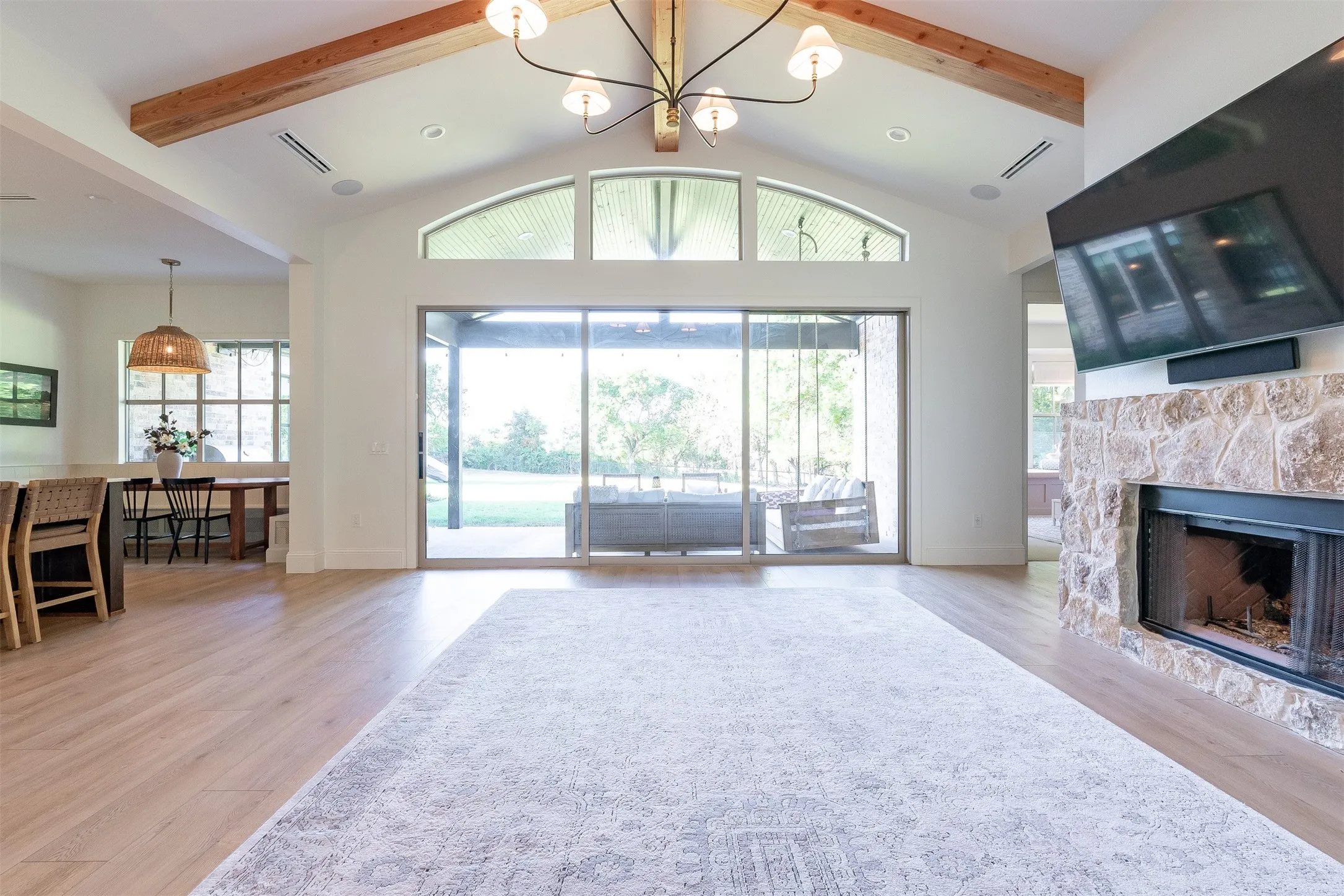 Vaulted ceiling with exposed wood beams, stone-clad fireplace, wood-finish flooring, and large sliding glass doors
