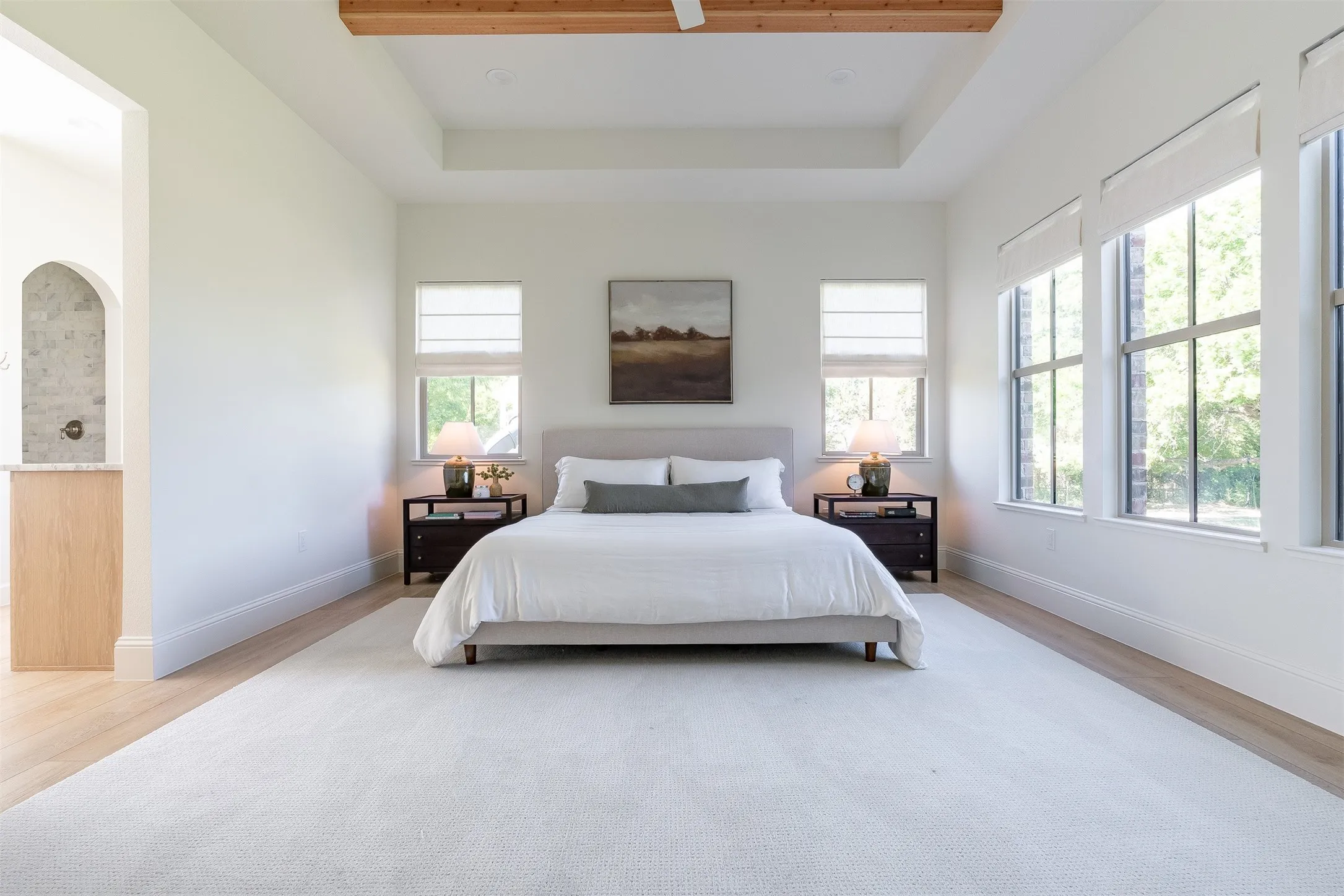 Tray ceiling with exposed wood beams, expansive floor-to-ceiling windows, light wood-finish flooring, and light-colored carpeting