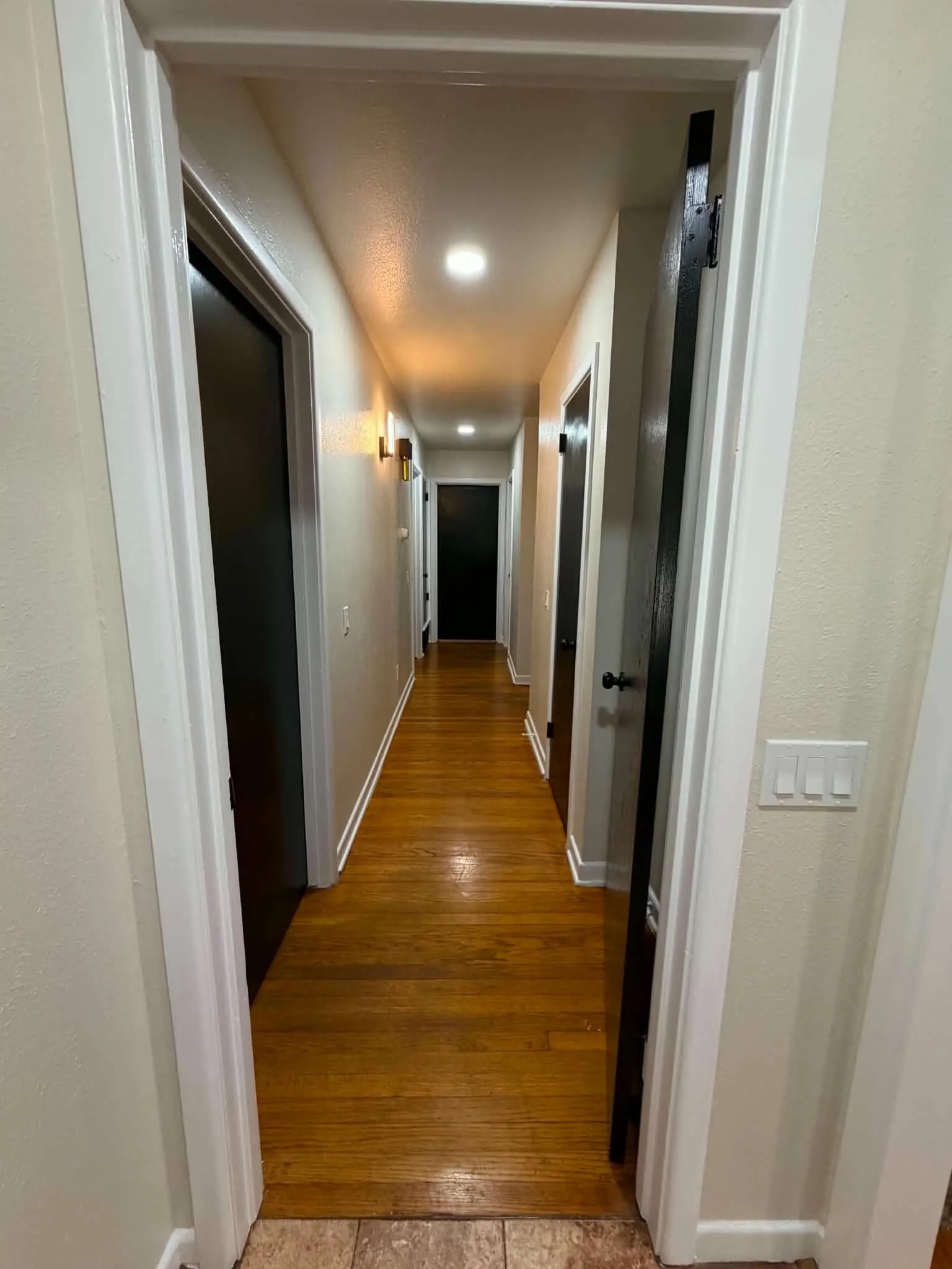 Hardwood flooring, recessed lighting, and wall-mounted sconces illuminate the hallway