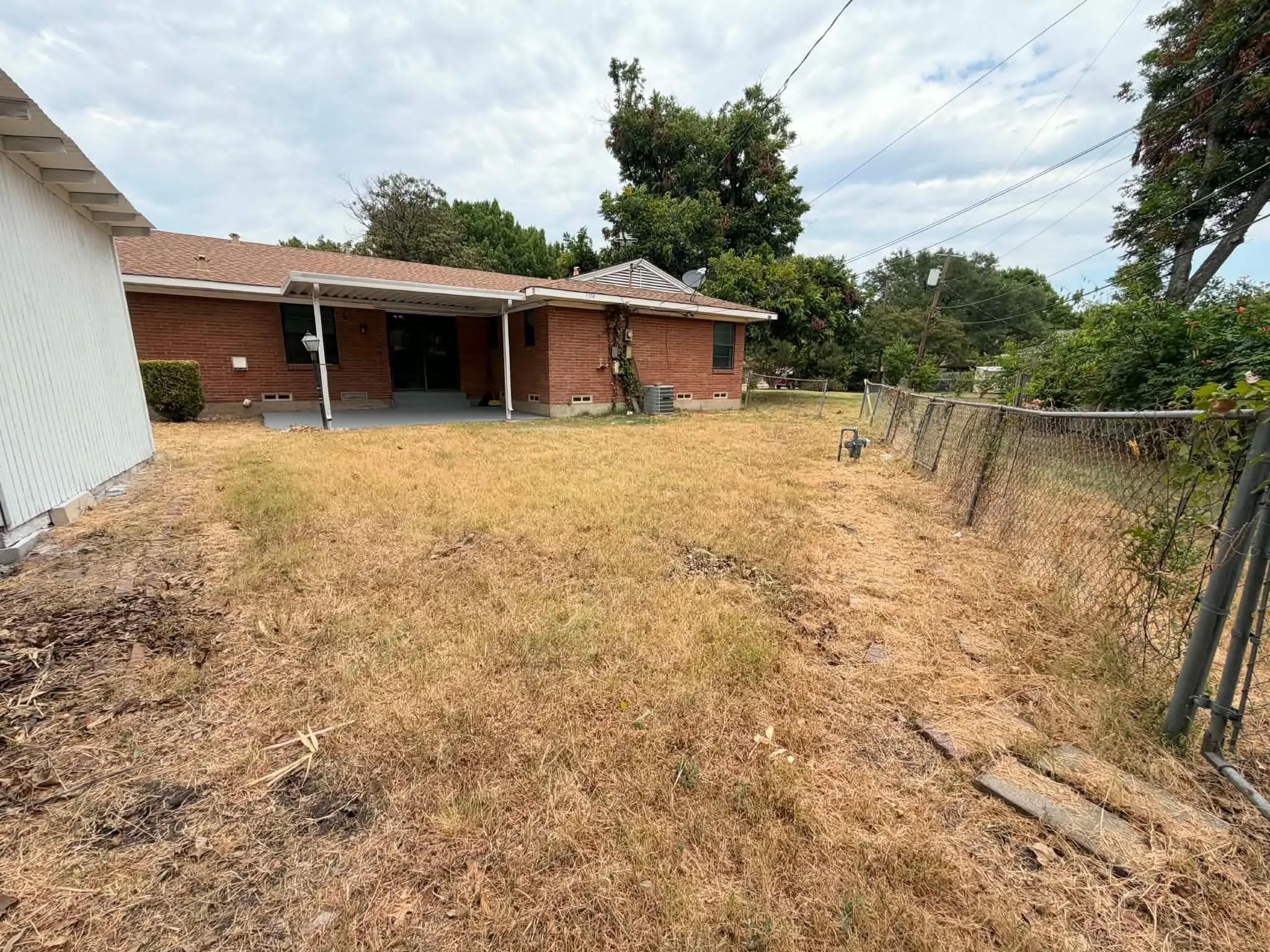 Expansive backyard featuring a chain-link fence, brick exterior, and a covered patio