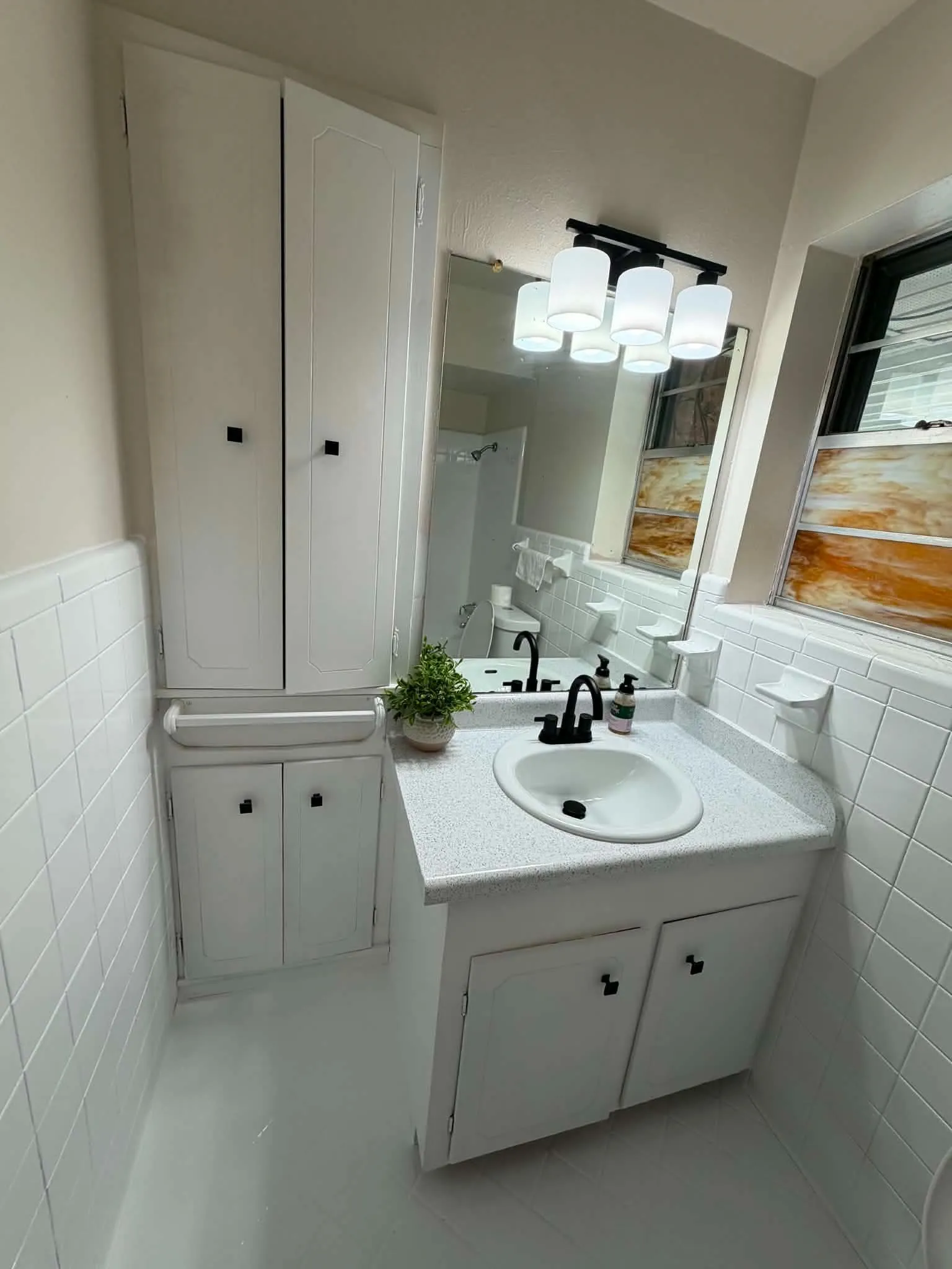 Built-in cabinetry, white tile walls, vanity with integrated sink, black hardware, and an overhead light fixture