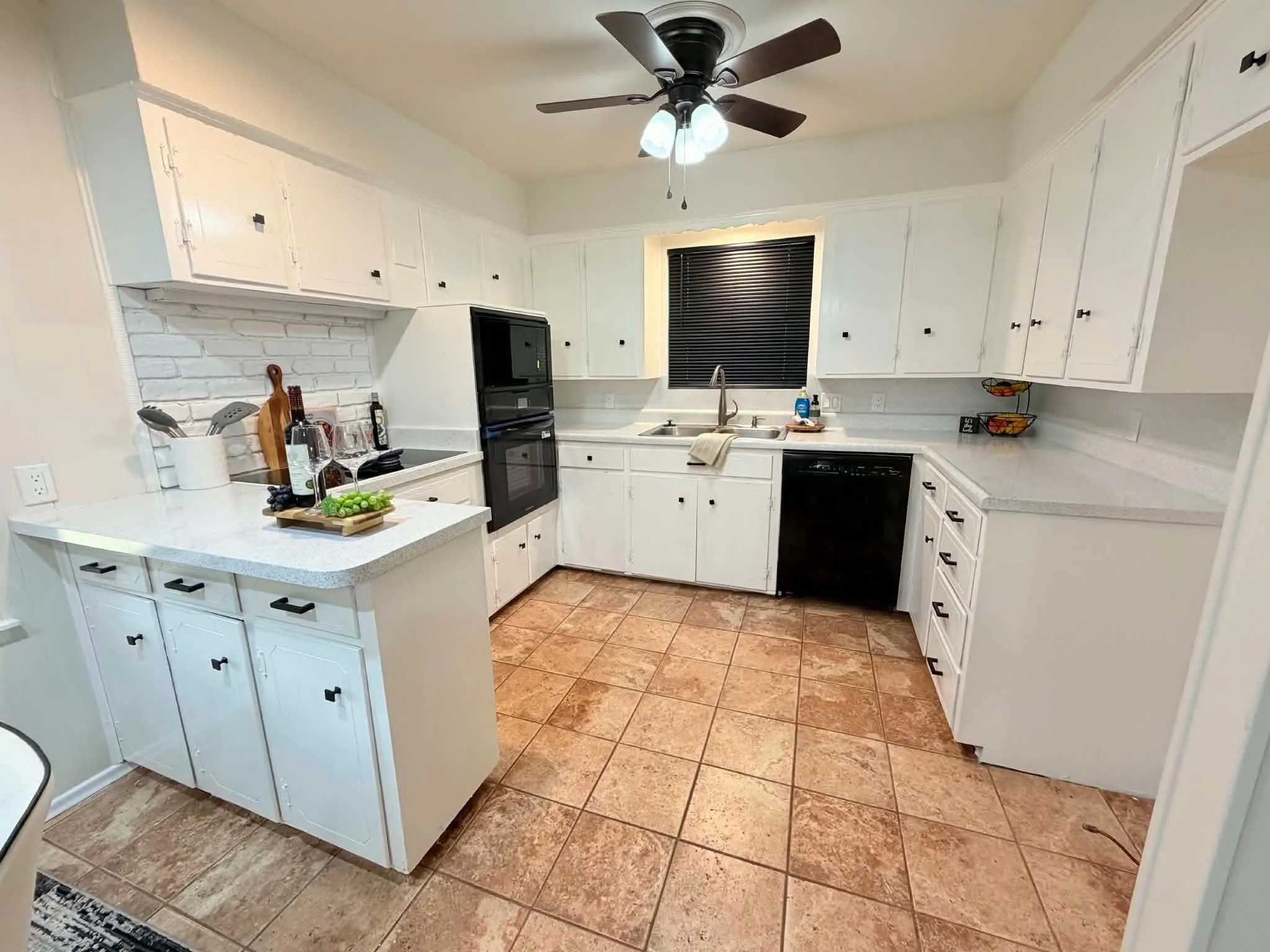 U-shaped kitchen with white cabinetry, built-in double oven, and tile flooring