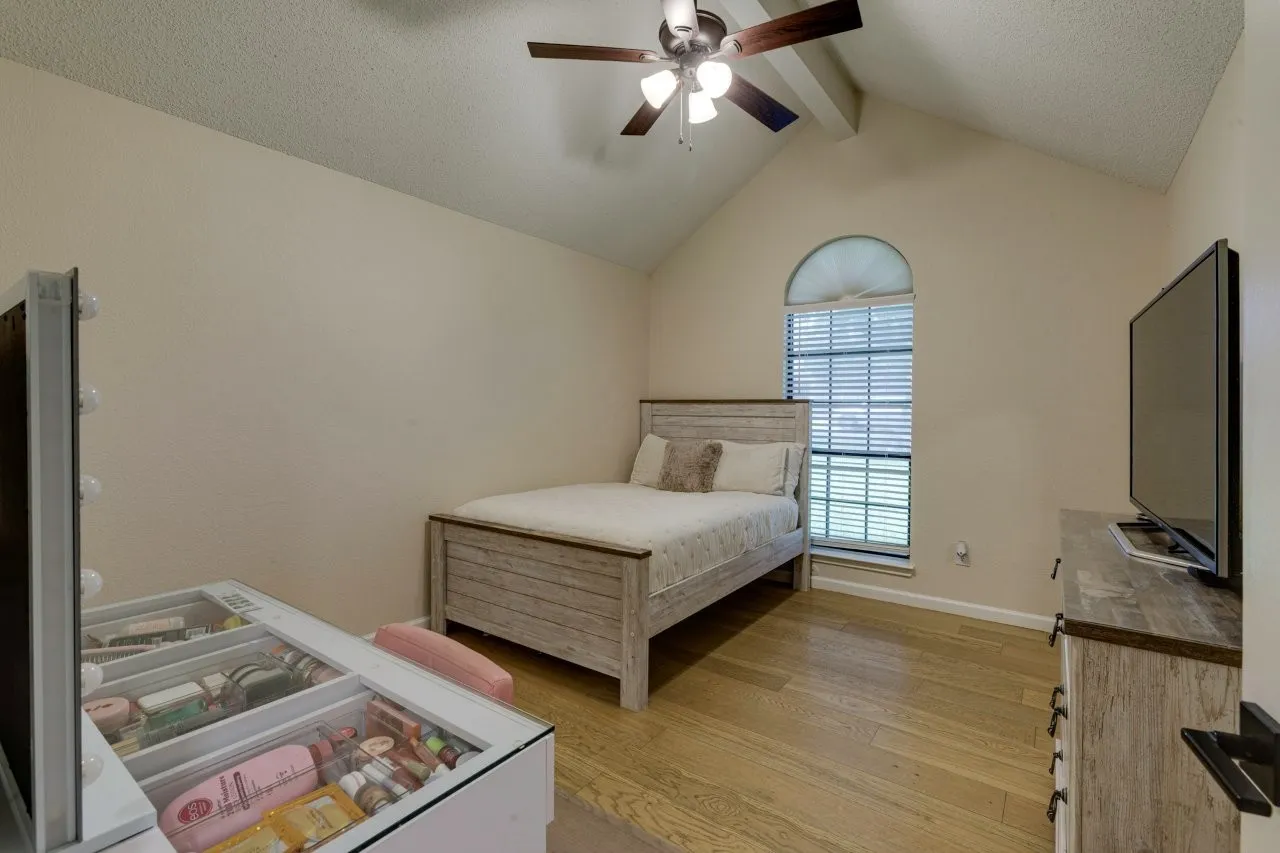 Vaulted ceiling with exposed beam, wood-finish flooring, ceiling fan with integrated lighting, and an arched window