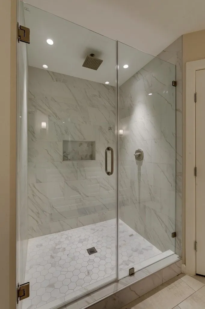 Glass-enclosed shower with a rainfall showerhead, tiled walls, hexagonal floor tiling, and an integrated shower niche