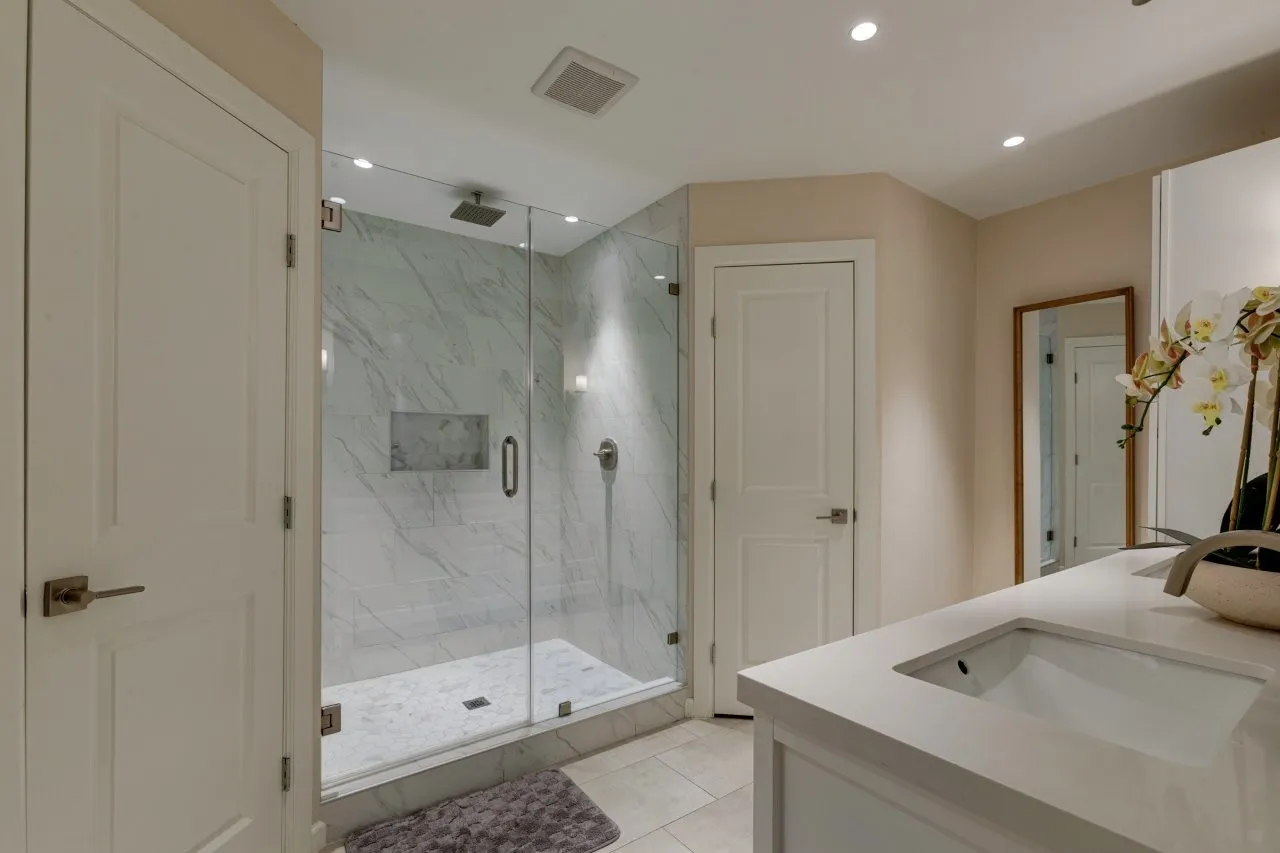 Glass-enclosed shower with marble-finish tile, integrated shower niche, and a rain shower head