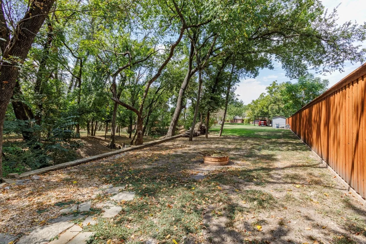 Expansive backyard featuring a wood fence, mature trees, and a fire pit