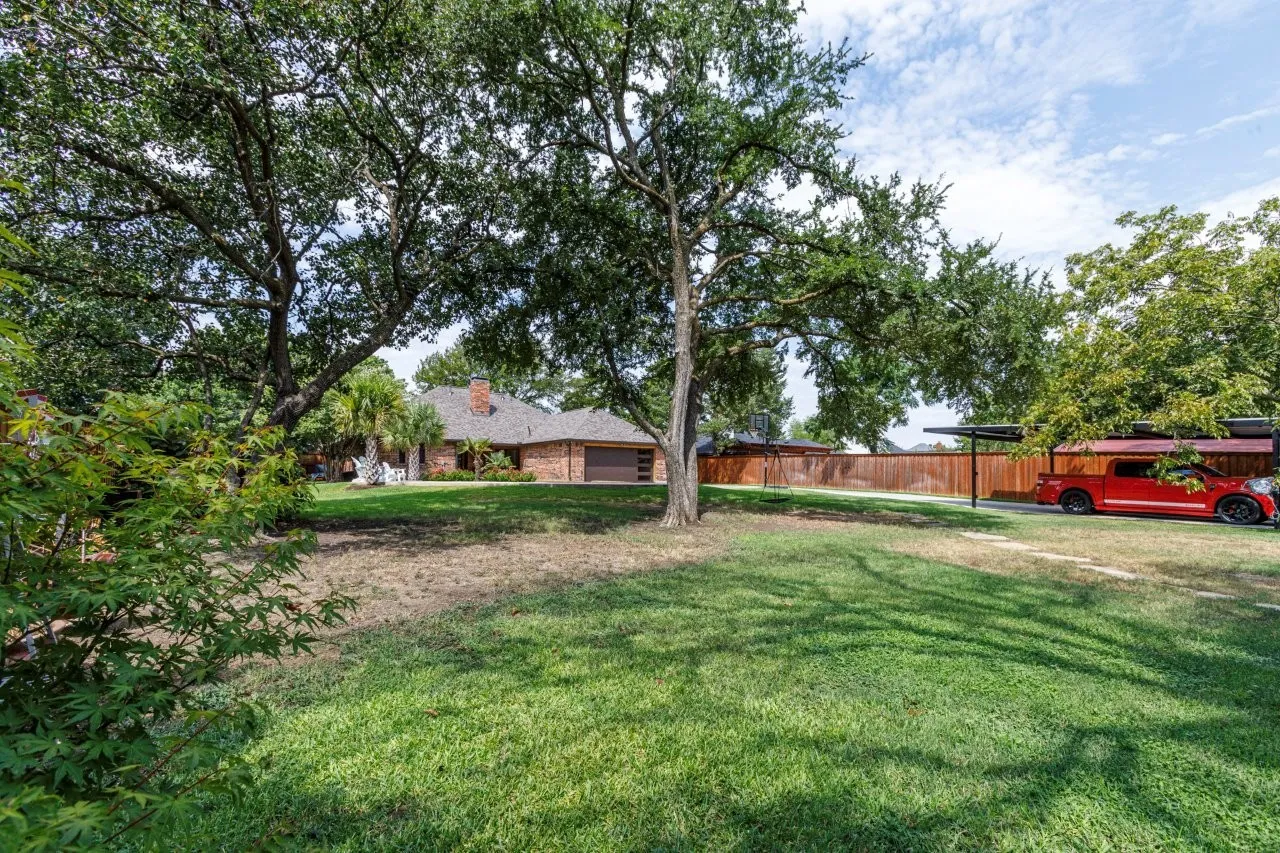Expansive front yard featuring mature trees, a brick-front residence, and an attached two-car garage