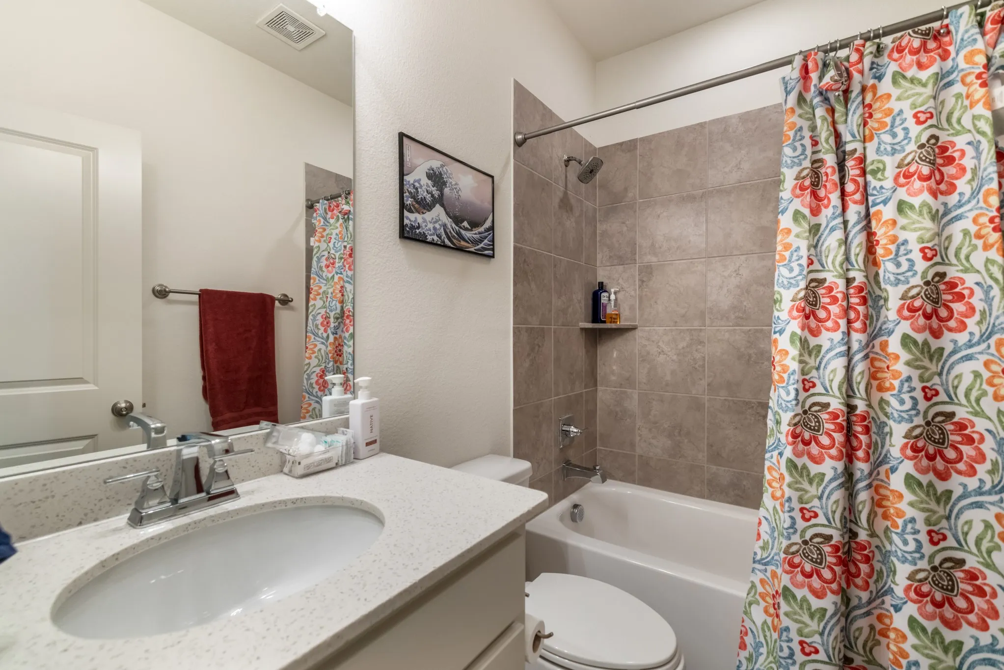 Bathroom featuring a single vanity with a white countertop, chrome faucet, full-width mirror, and a bathtub with tile surround