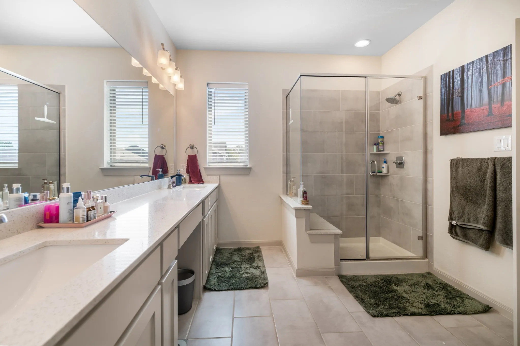 Dual vanity with integrated sinks, expansive counter space, a glass-enclosed shower, built-in shower shelving, and tile flooring