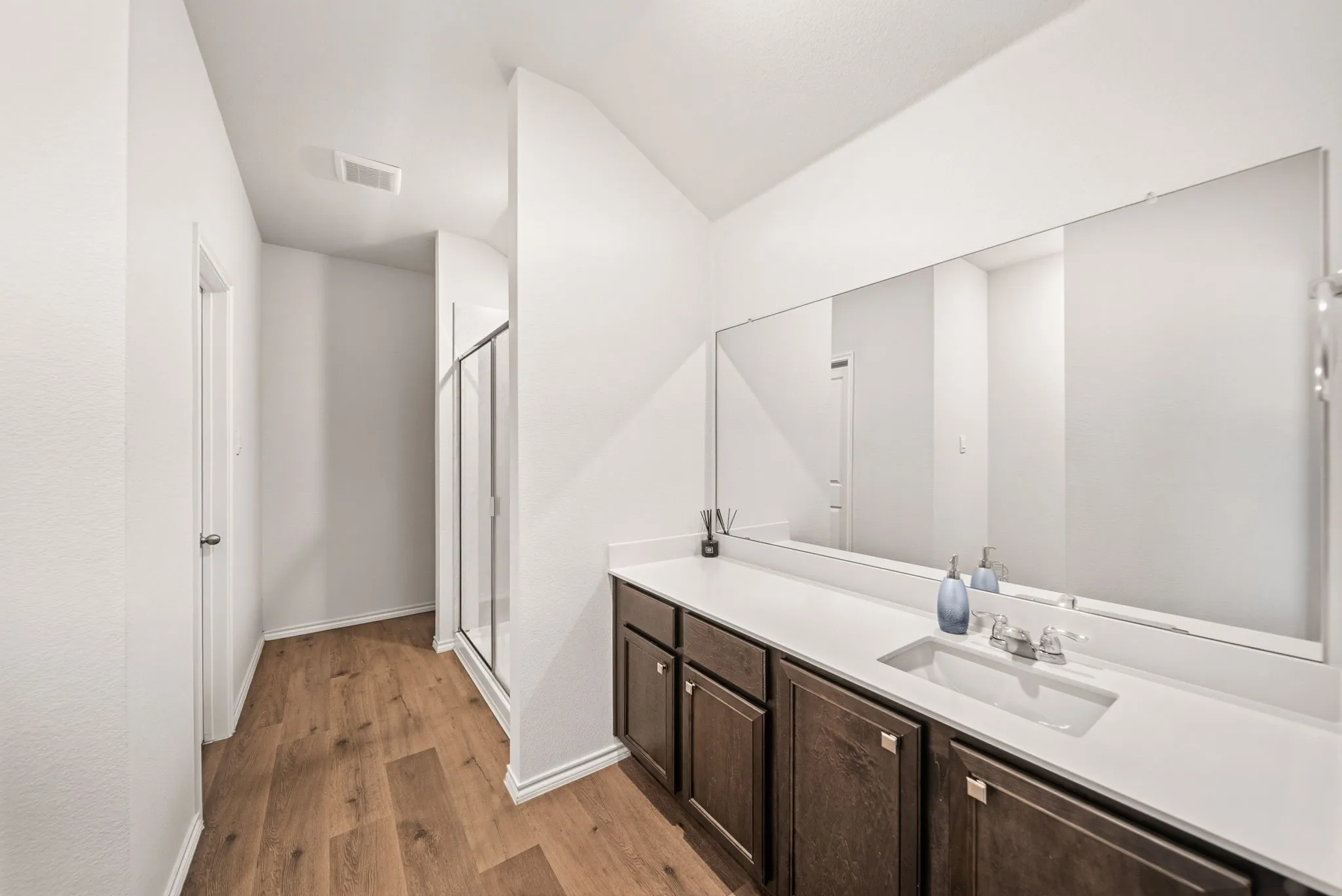Wood-finish flooring with a vanity featuring a single sink, dark wood cabinetry, and a full-width mirror