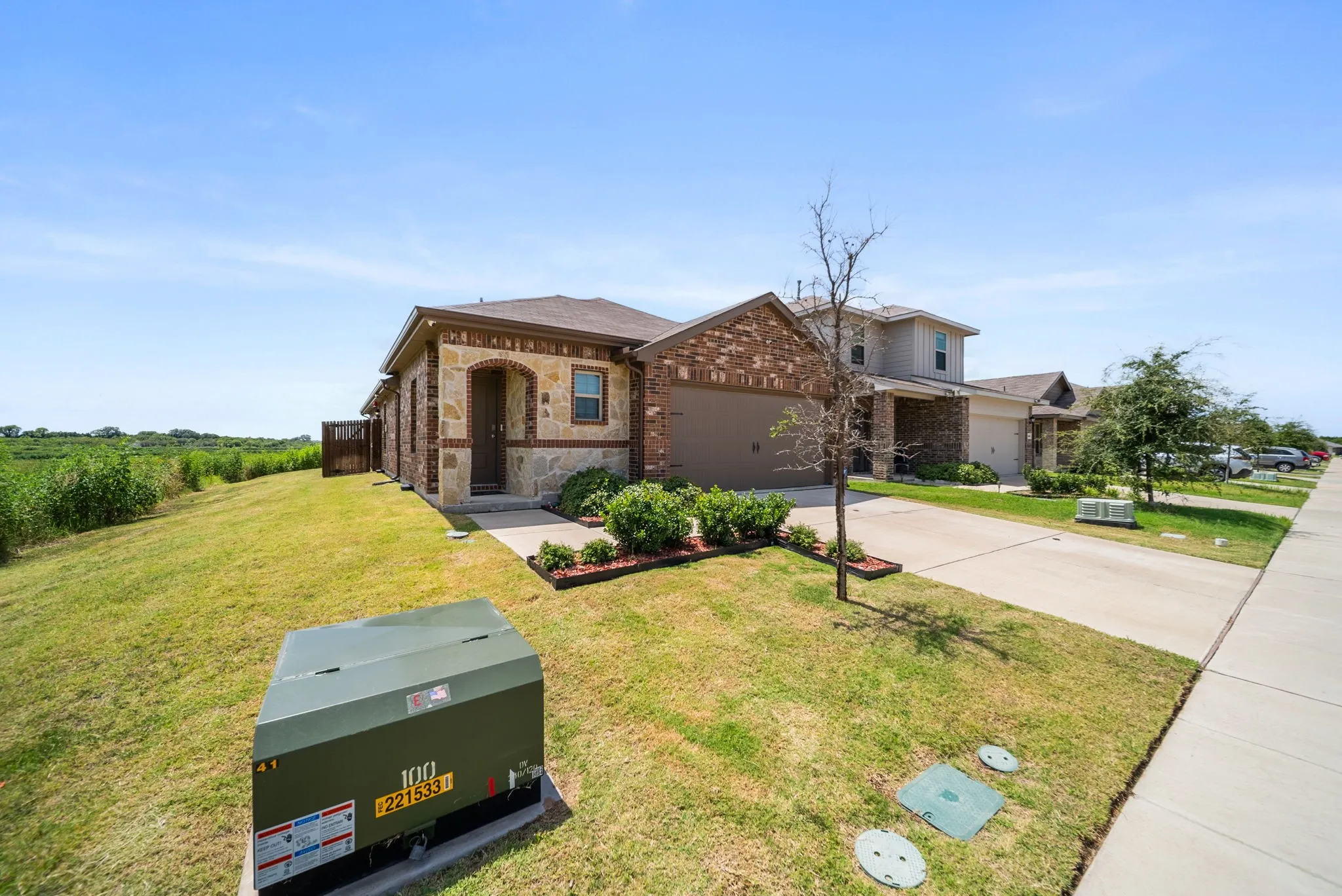 Brick and stone facade, attached garage, concrete driveway, front yard landscaping, and a side fence
