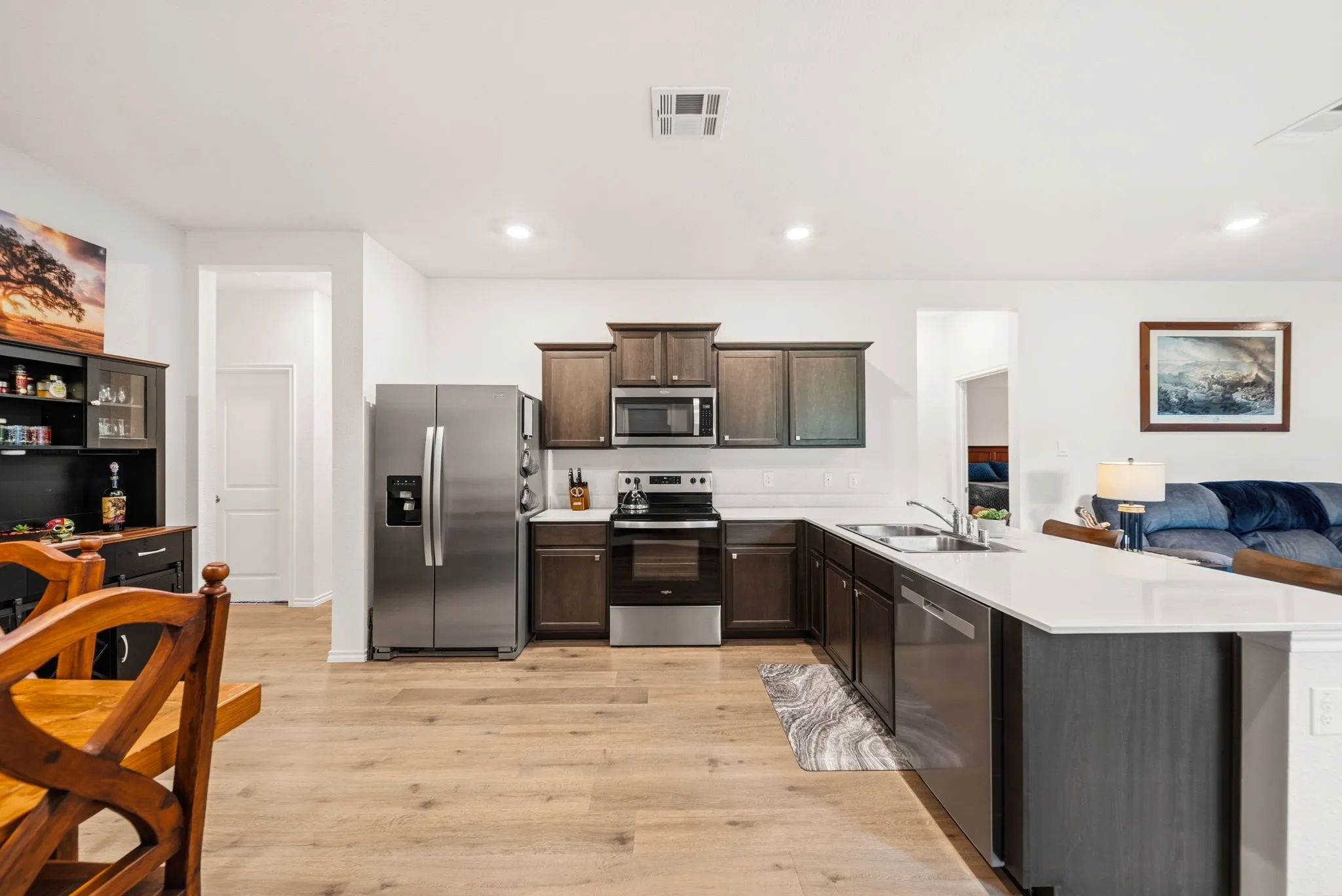 Modern kitchen featuring wood-finish flooring, stainless steel appliances, dark wood-finish cabinetry, a white subway tile backsplash, and a white countertop