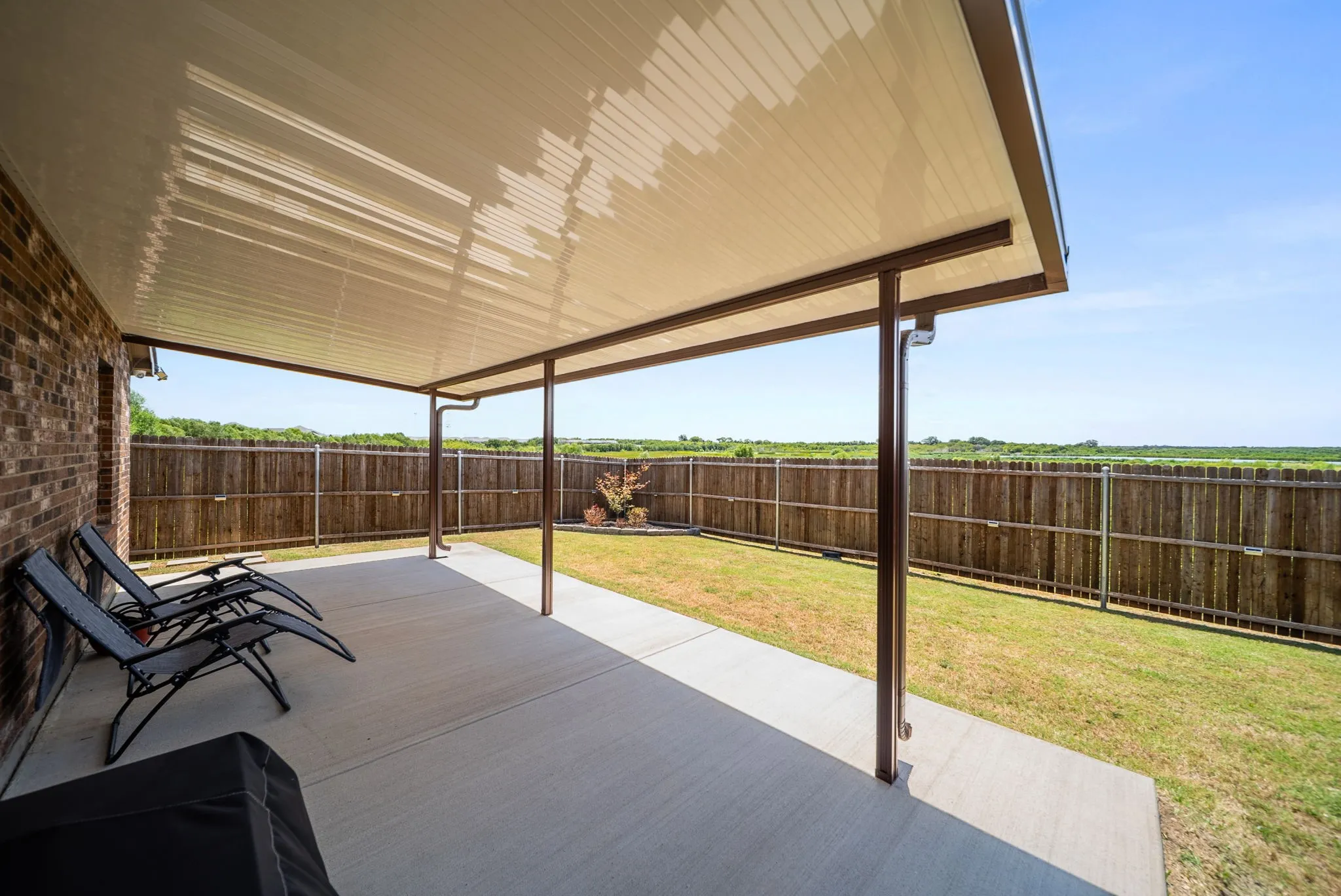 Expansive concrete patio with a covered overhead structure, brick exterior, and a fenced backyard