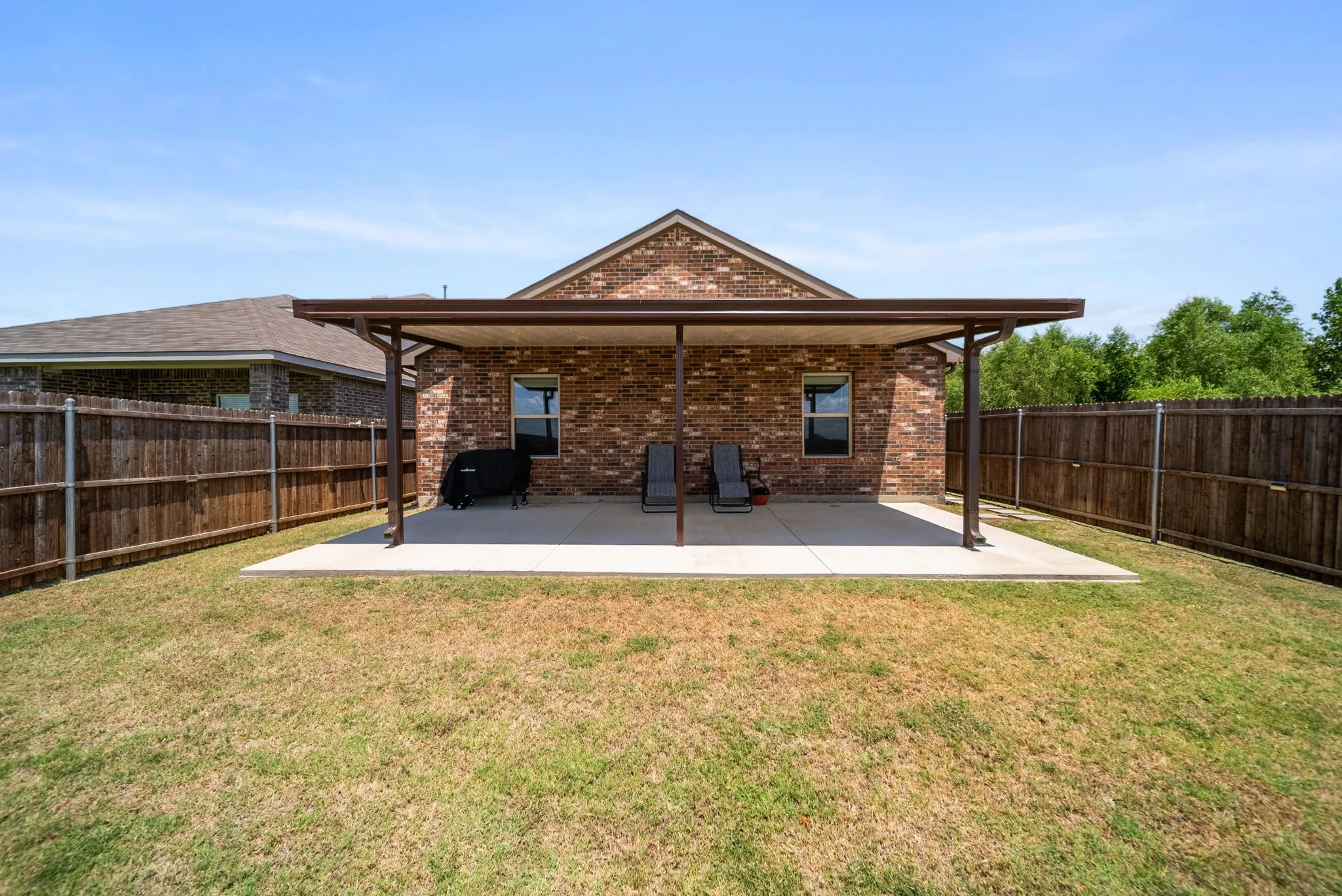 Expansive backyard featuring a covered patio, brick exterior, and wood fencing