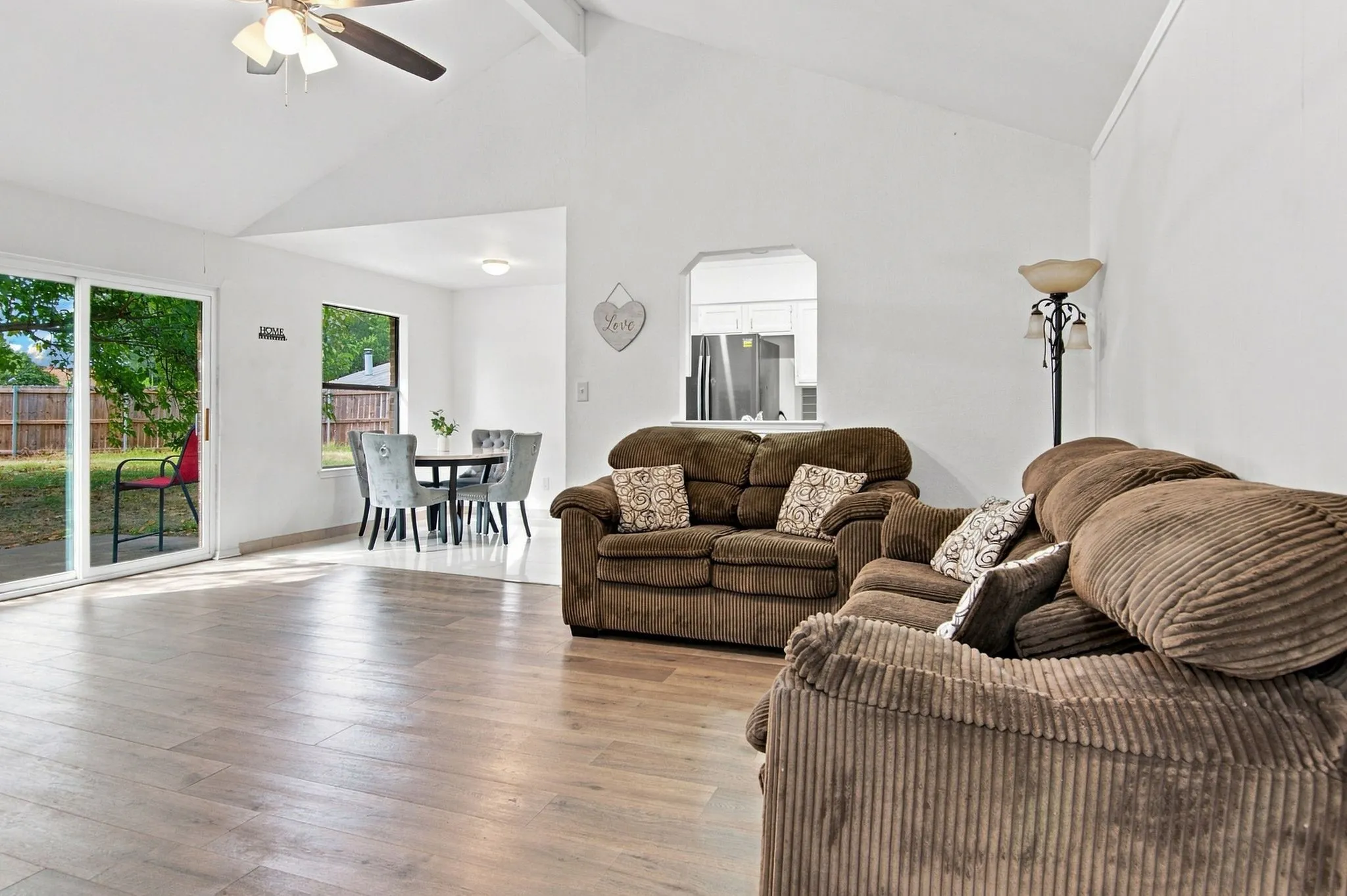 Vaulted ceilings with a ceiling fan, wood-finish flooring, sliding glass doors, and a pass-through window to the kitchen