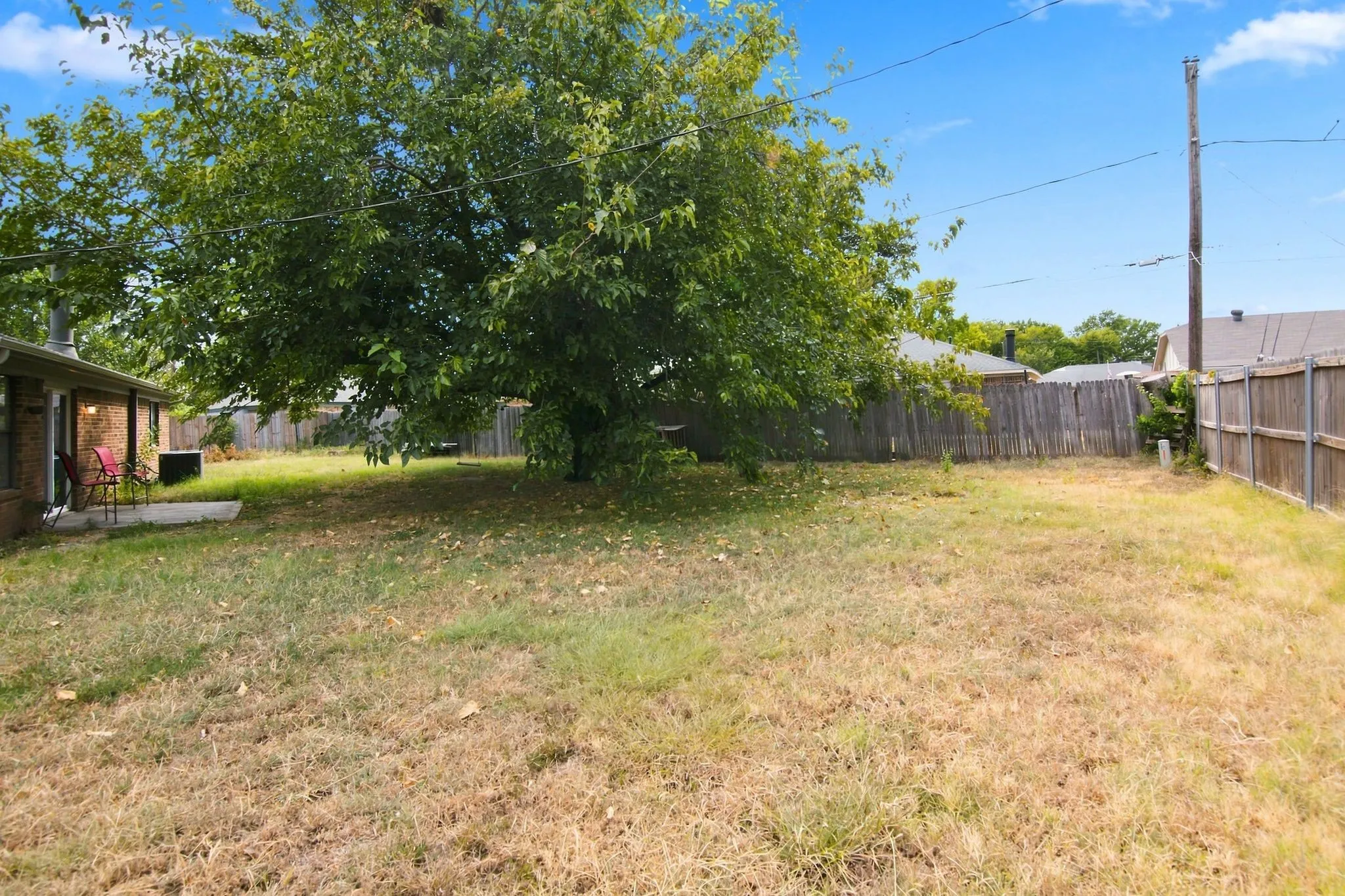 Expansive backyard featuring a mature tree, wooden privacy fencing, and a concrete patio