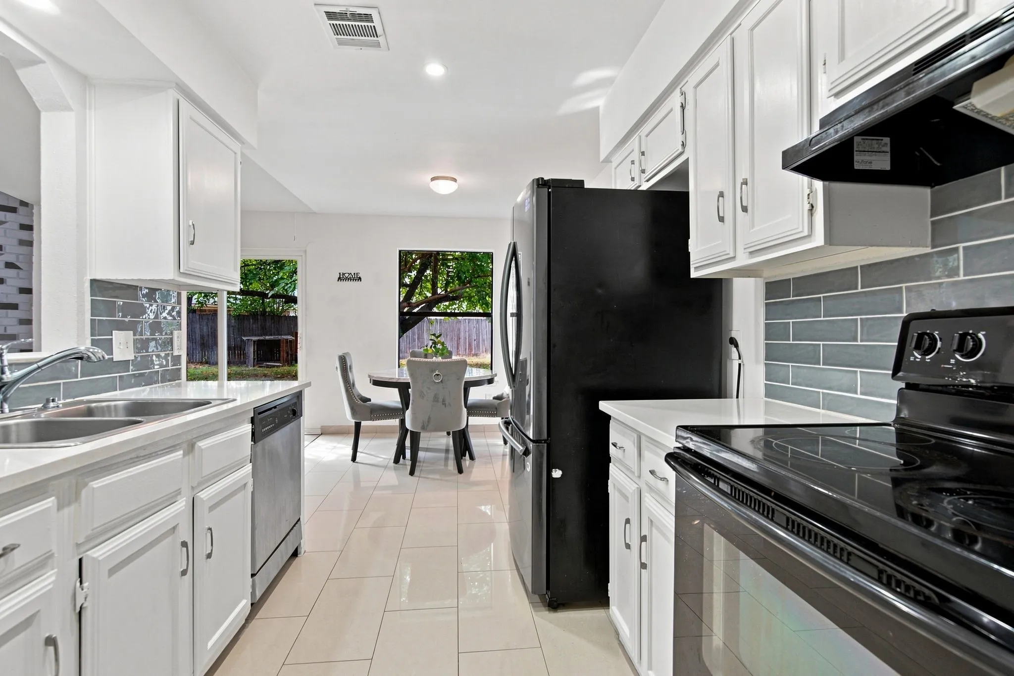 White cabinetry, light countertops, subway tile backsplash, stainless steel sink, and black appliances