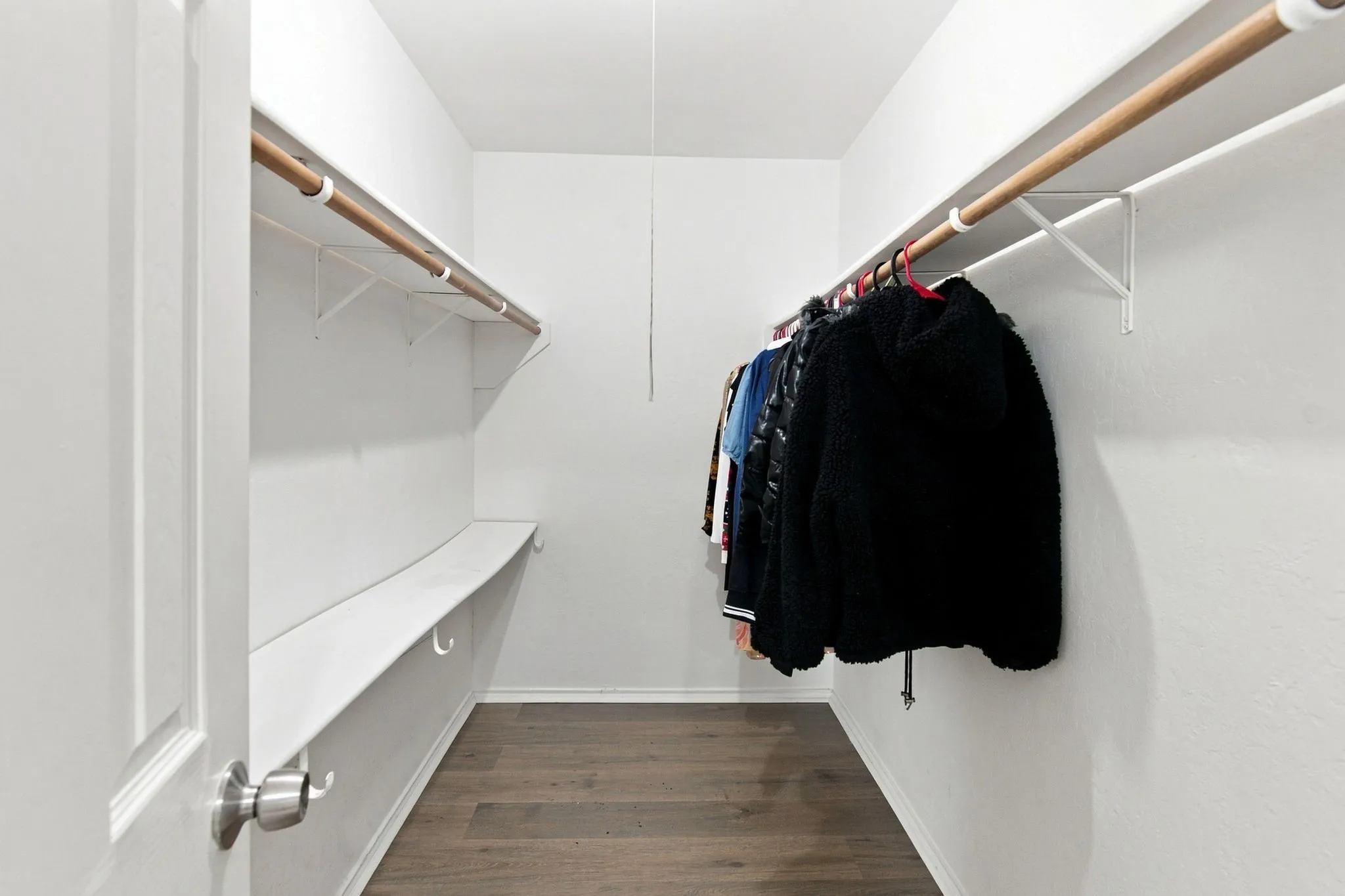 Walk-in closet with wood-finish flooring, white walls, and built-in shelving