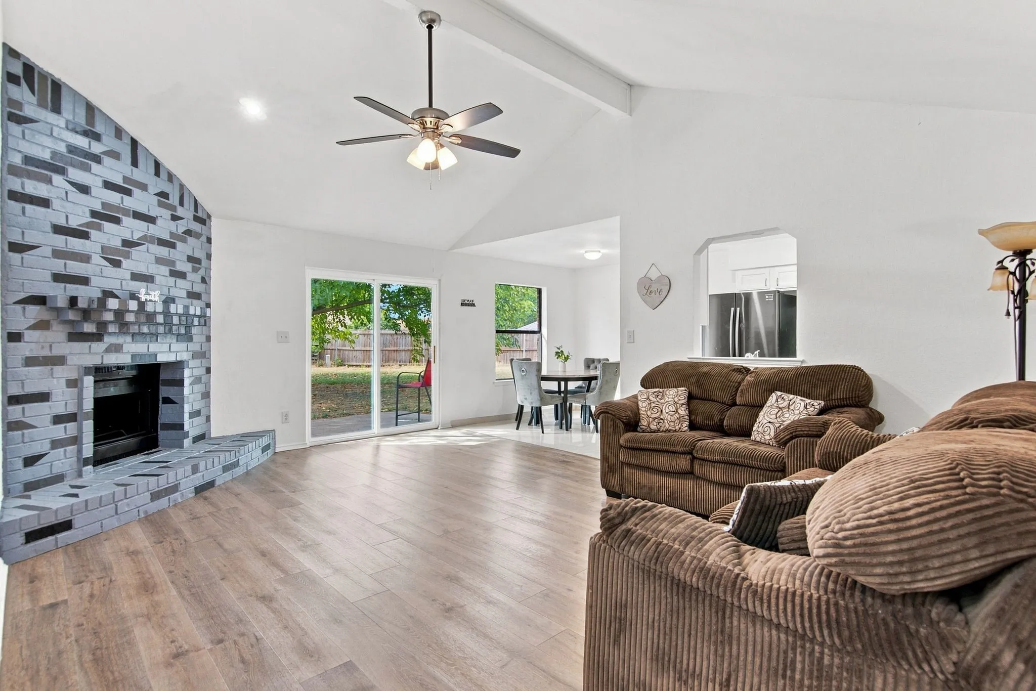 Vaulted ceiling with exposed beams, wood-finish flooring, and a brick fireplace