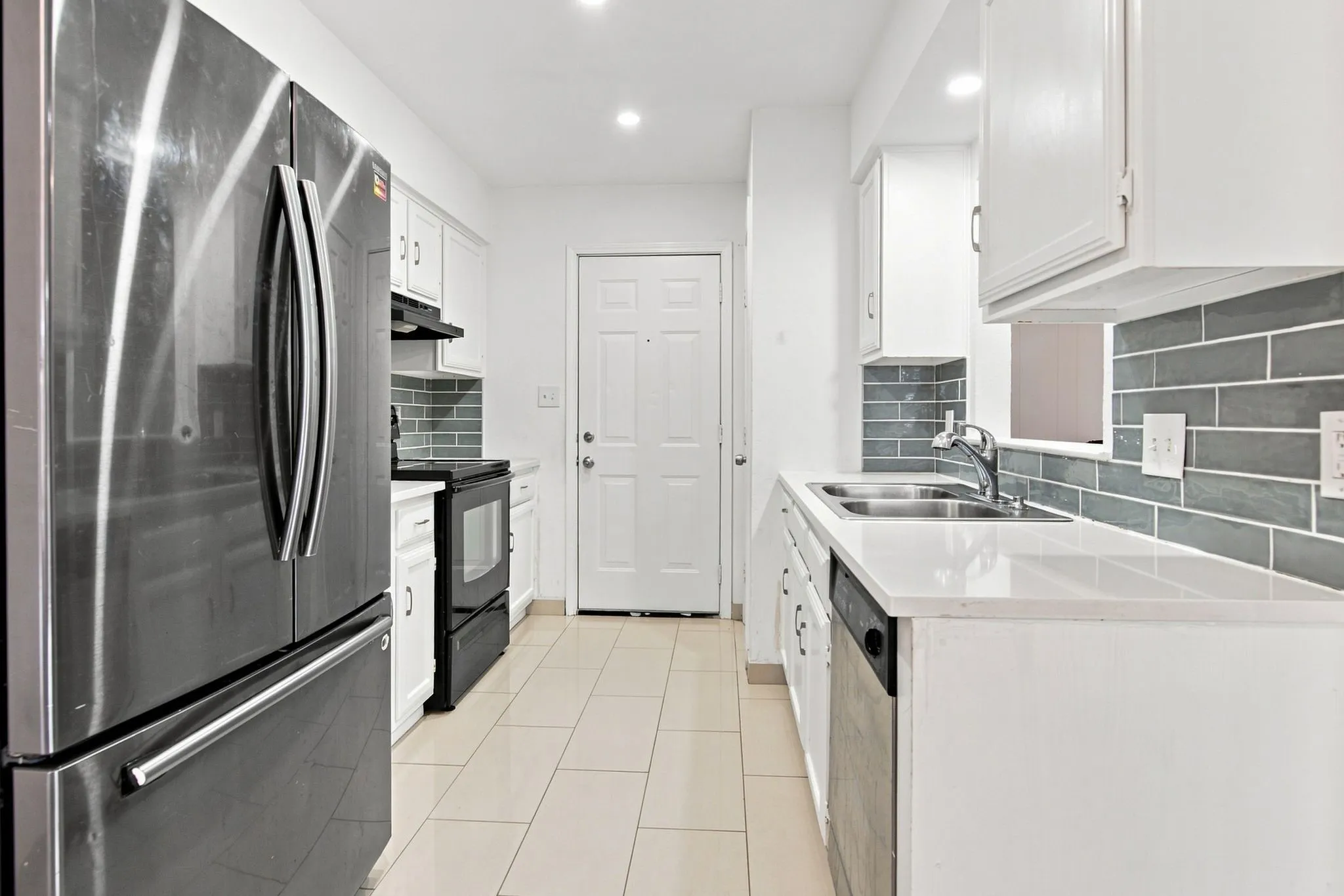 Stainless steel refrigerator and dishwasher, white cabinetry, solid surface countertops, subway tile backsplash, and tile flooring