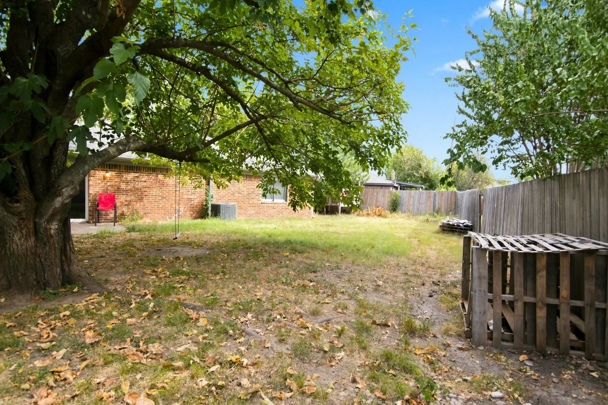 Expansive backyard featuring mature trees, a brick-clad exterior, and a wood privacy fence
