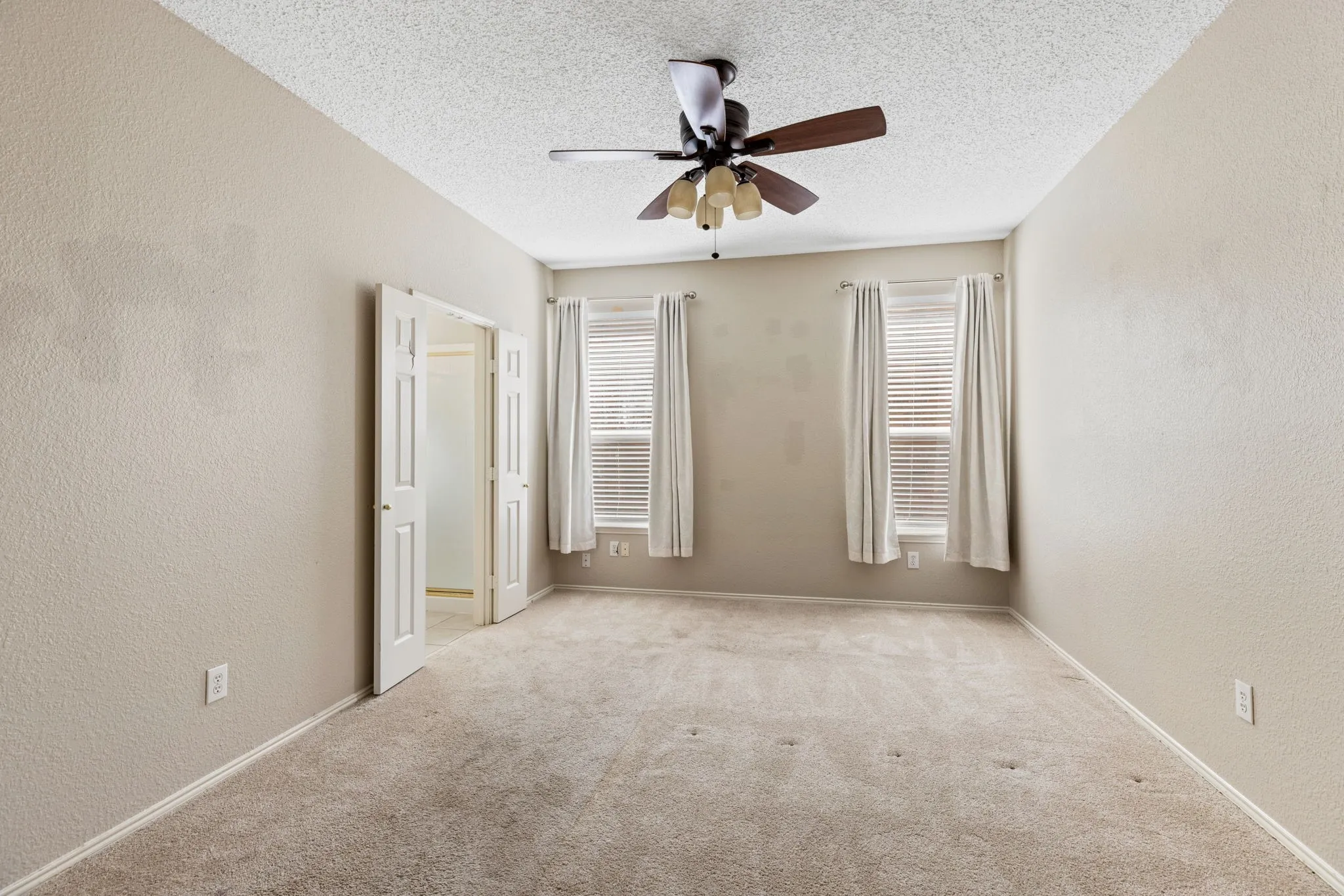 Carpeted flooring, dual windows with blinds, ceiling fan with light fixture, double French doors, and neutral wall tones