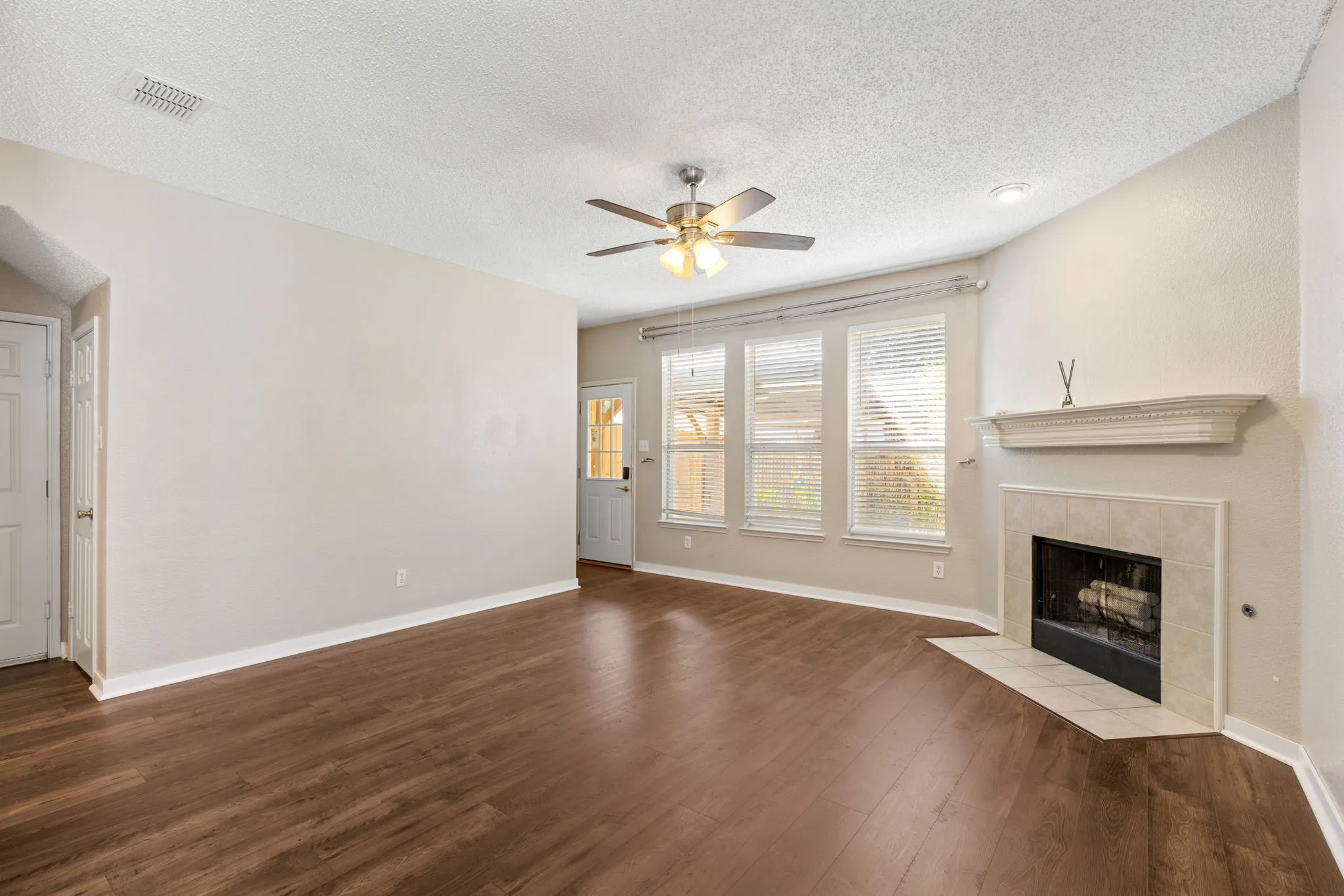 Spacious room with wood-finish flooring, a ceiling fan, and a fireplace with a decorative mantel and tiled hearth