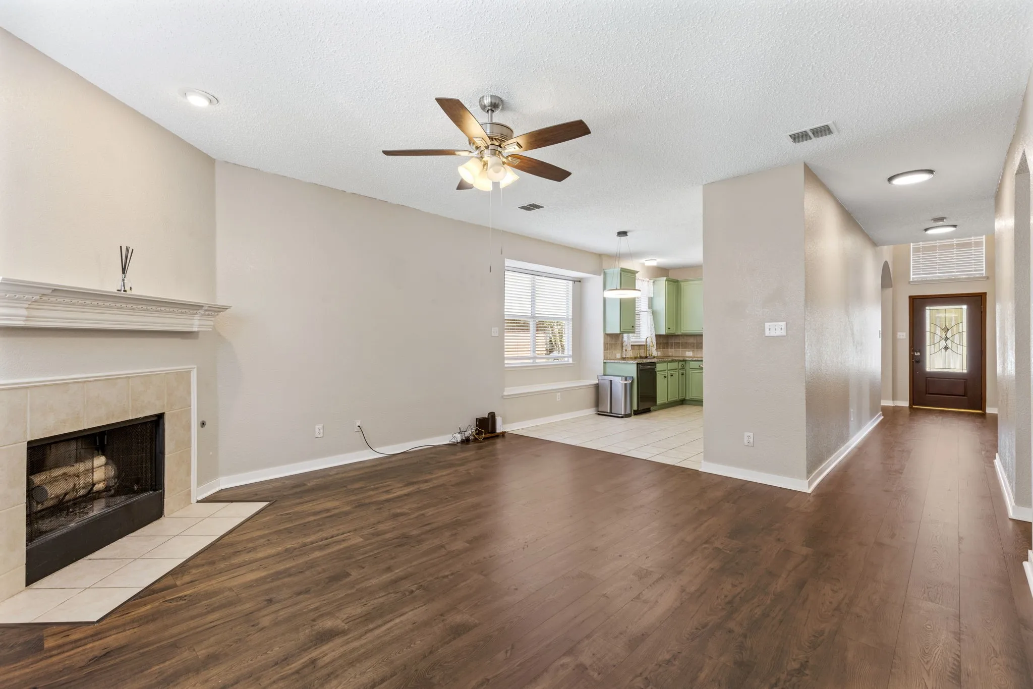 Vaulted ceiling with recessed lighting and ceiling fan, wood-finish flooring, tile-surround fireplace with mantel, and a front entry door with decorative glass inserts