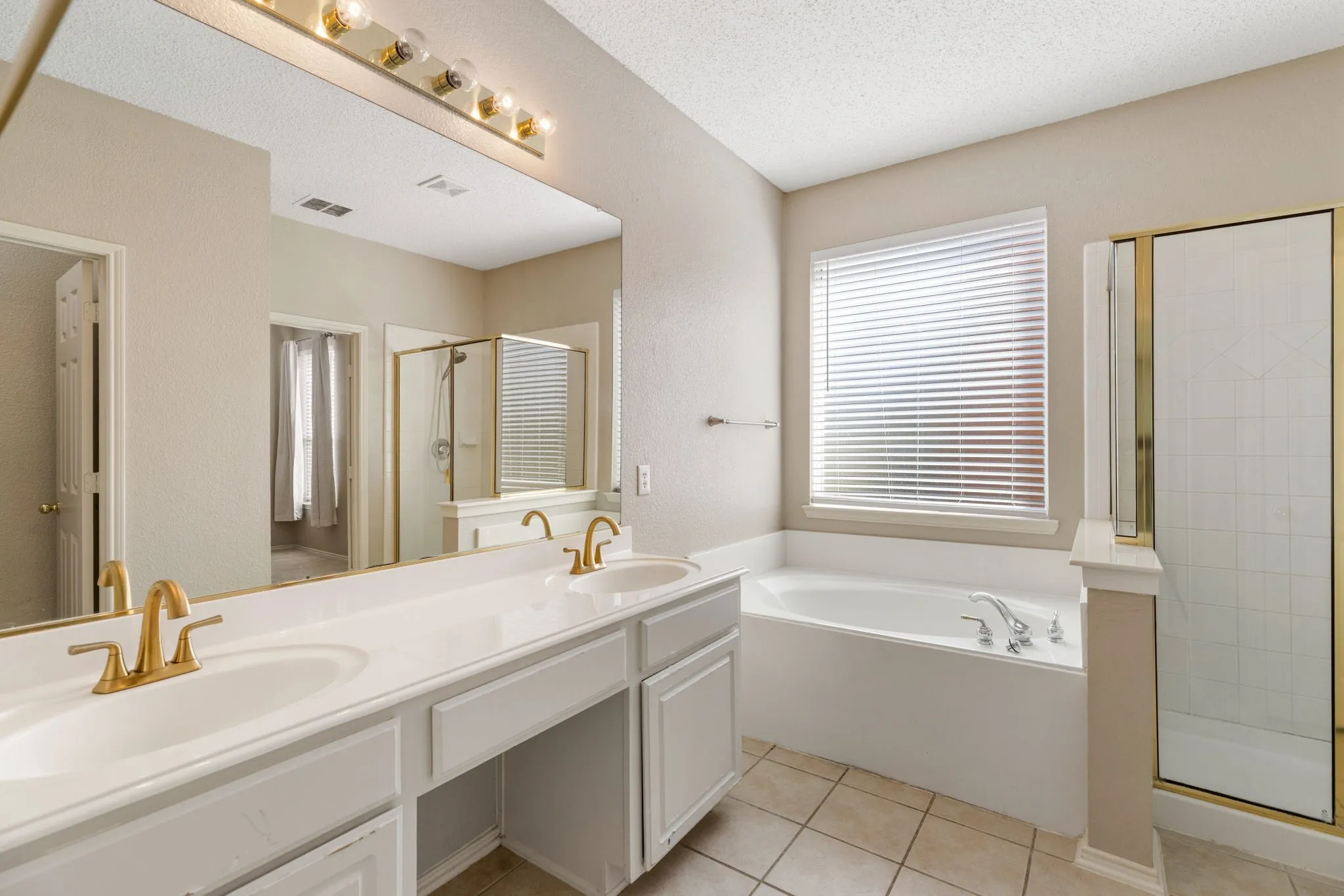 Dual vanity with gold-tone hardware, large framed mirror, built-in soaking tub, and enclosed shower with gold-tone framing