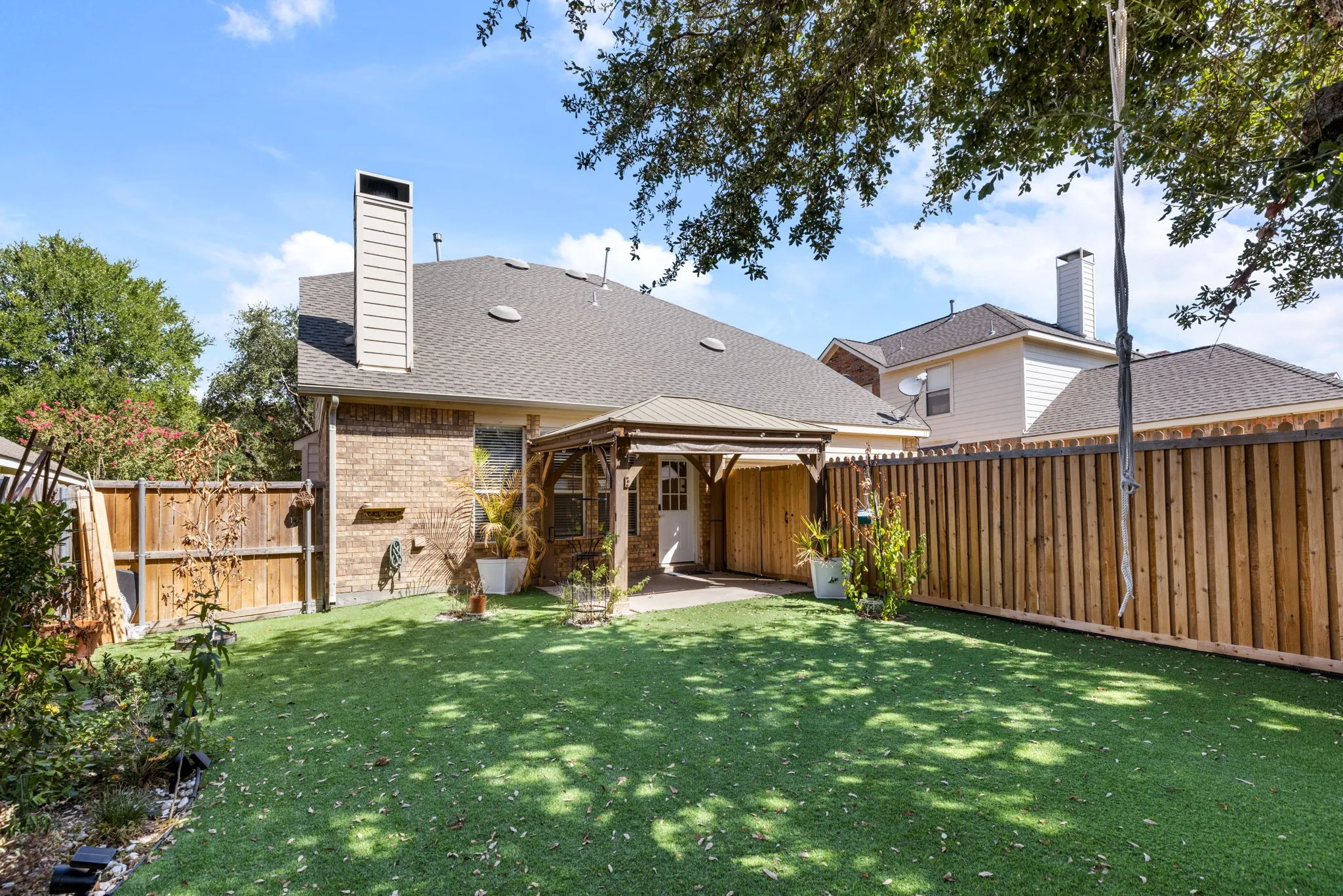 Expansive backyard featuring artificial turf, a wood privacy fence, a brick exterior, and a covered patio with a pergola