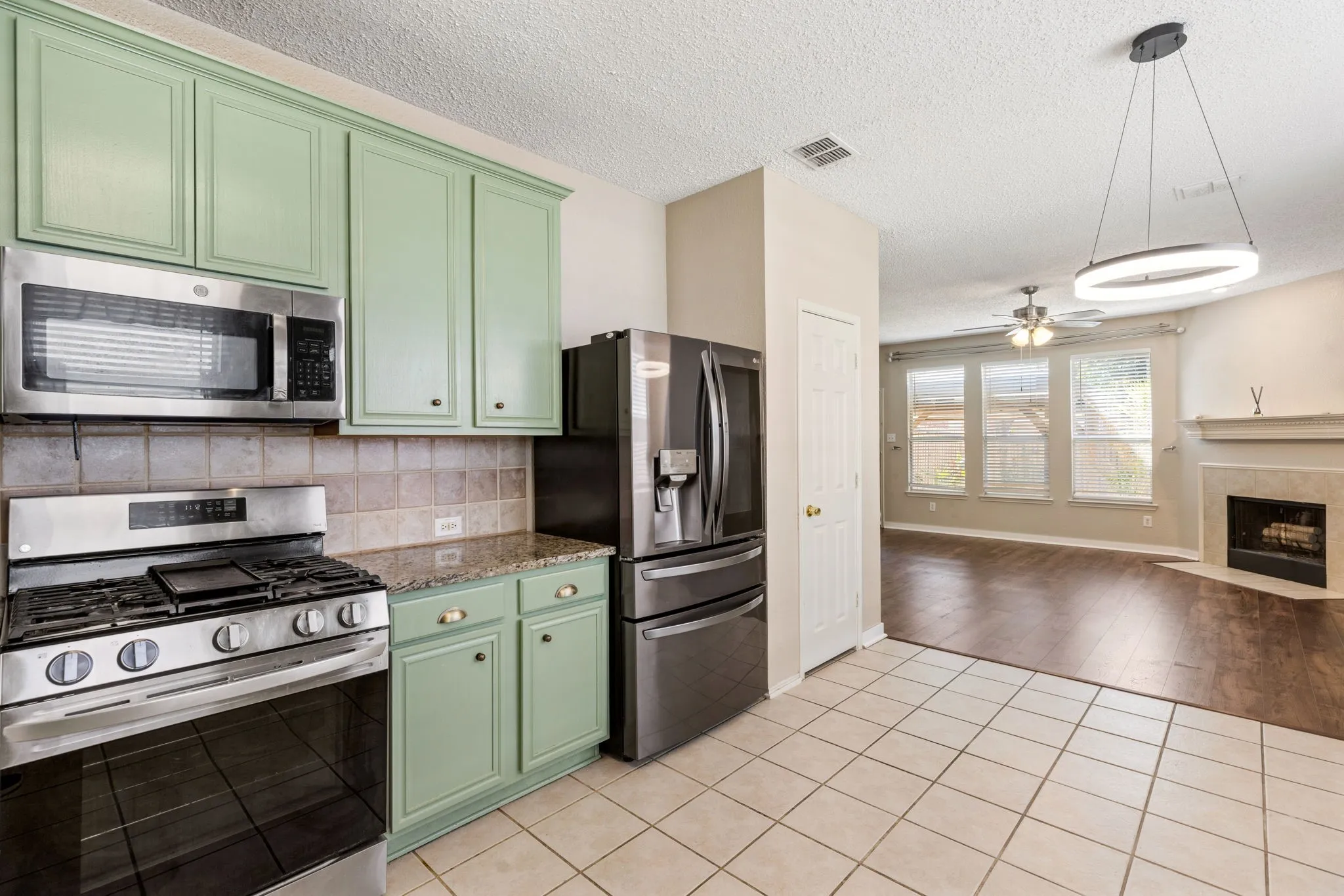 Kitchen featuring stainless steel appliances, green cabinetry, tile backsplash, and stone countertops