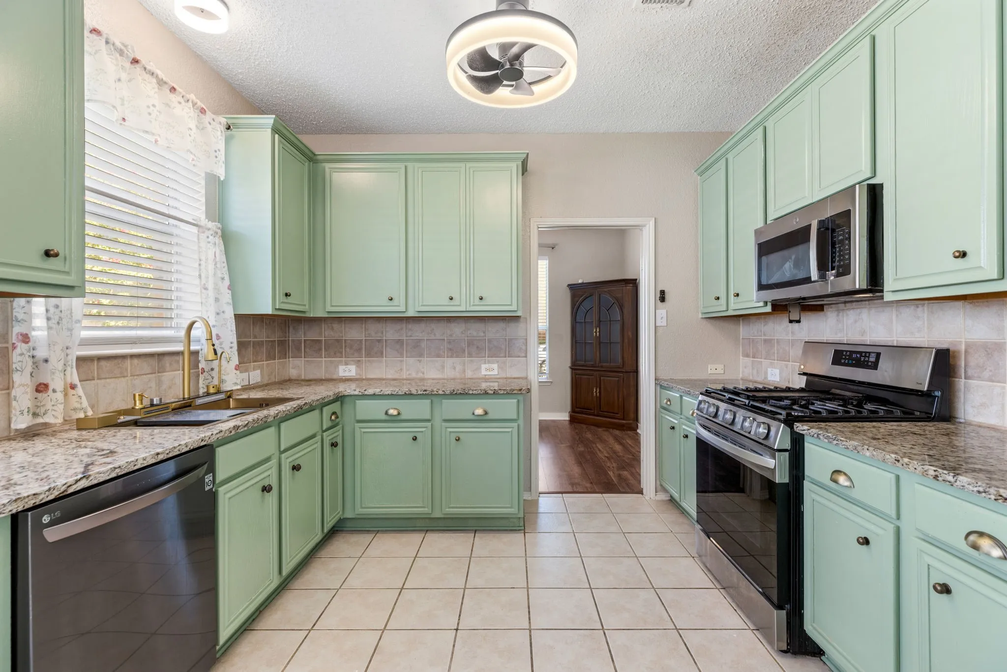Kitchen featuring light green cabinetry, granite countertops, stainless steel appliances, tile flooring, and a tile backsplash