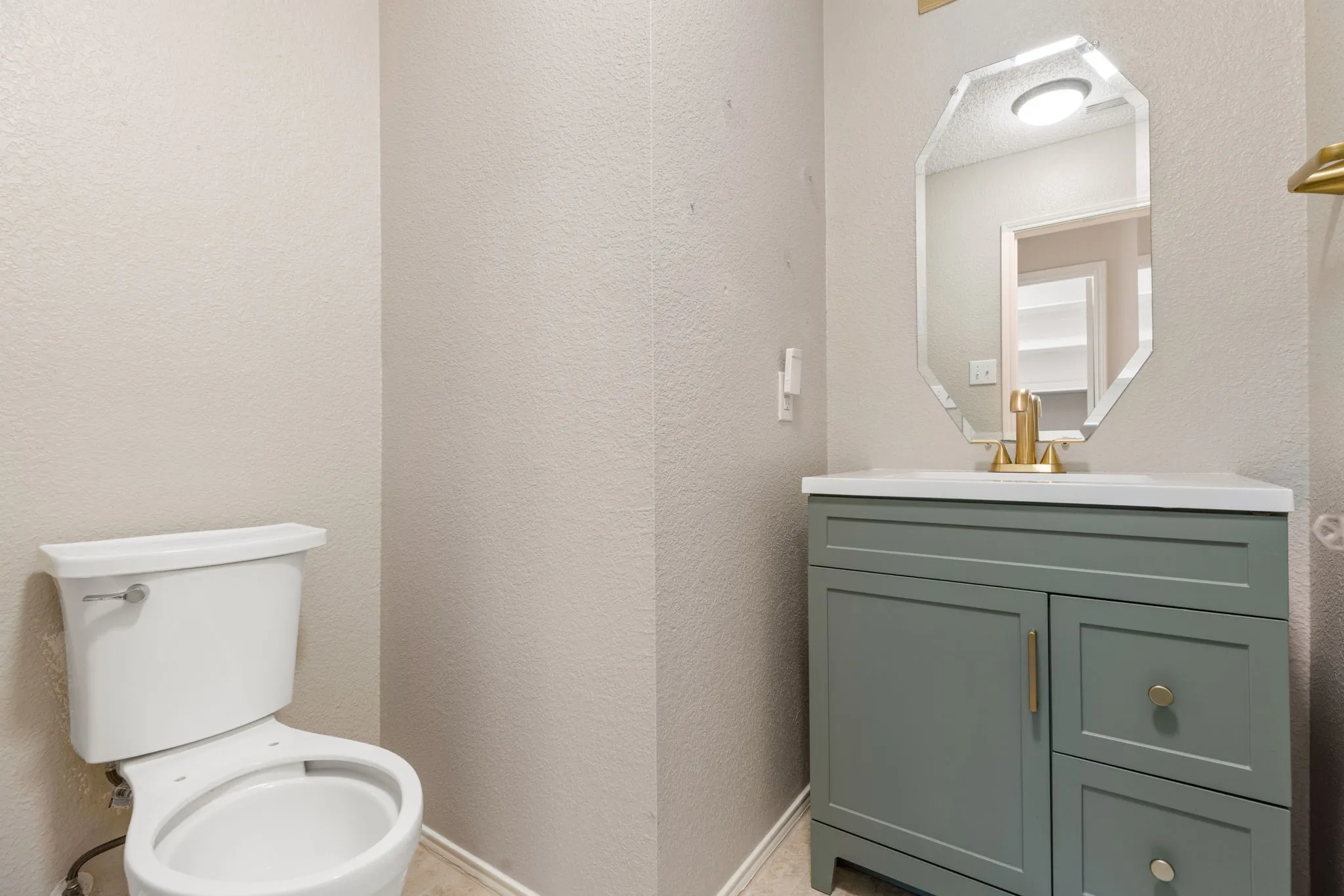 Bathroom featuring a contemporary vanity with a white countertop, gold-toned faucet, and a decorative octagonal mirror