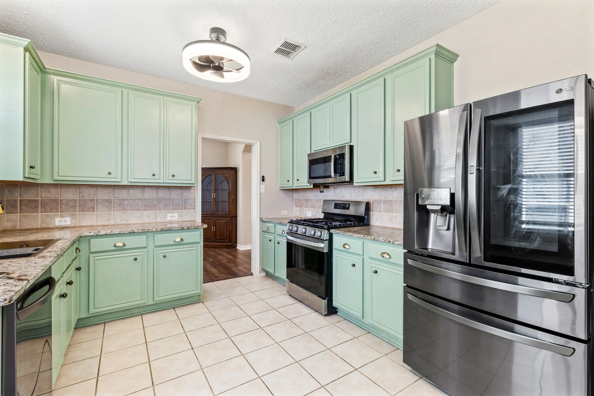 Kitchen featuring light green cabinetry, tile flooring, granite countertops, and stainless steel appliances