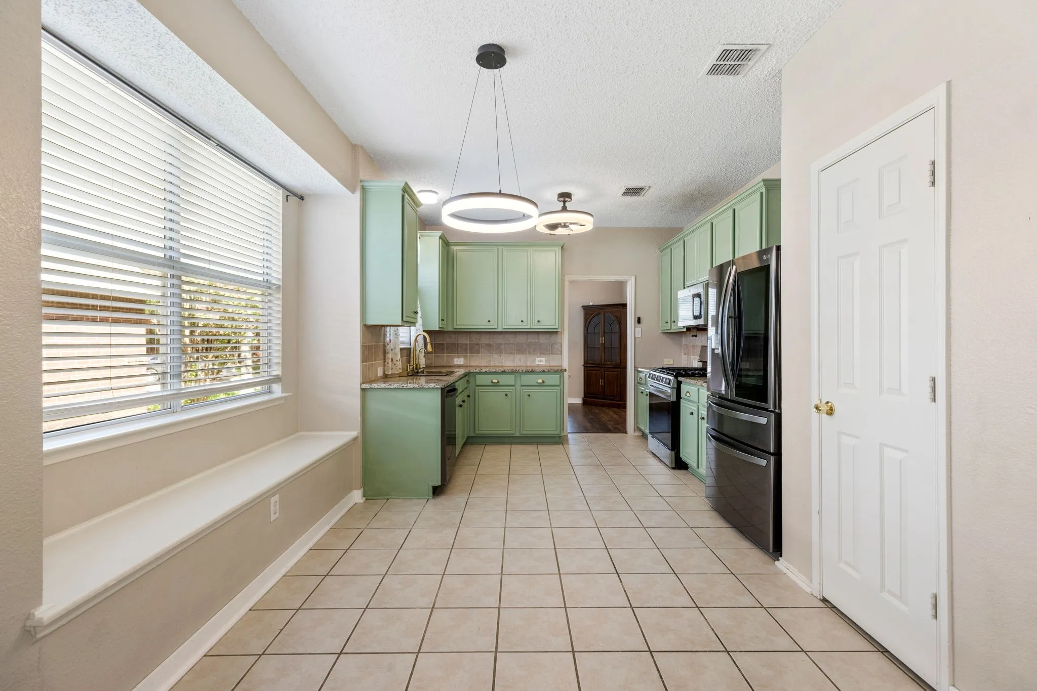 Kitchen featuring sage green cabinetry, stone countertops, stainless steel appliances, and tile flooring