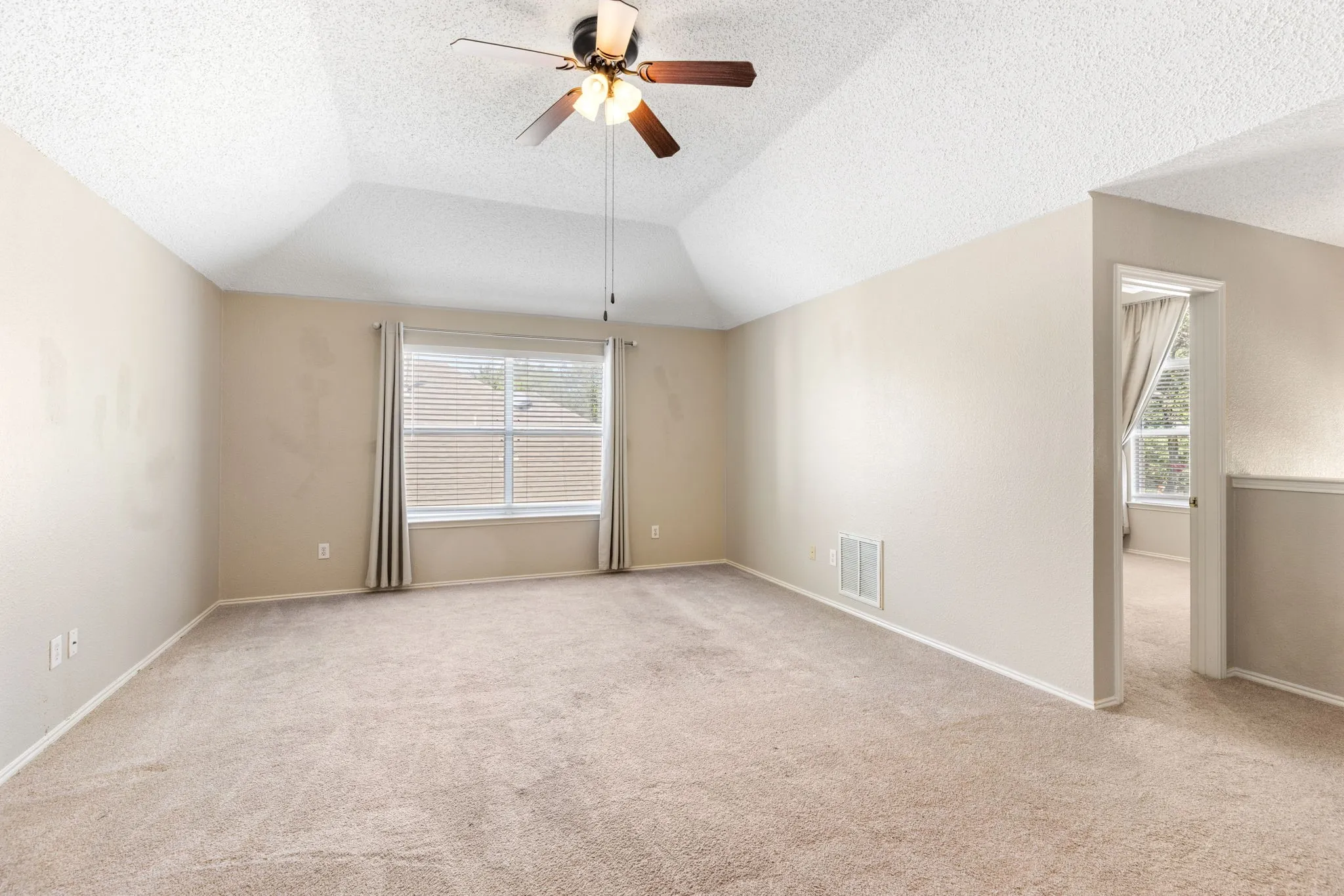 Carpeted room featuring a vaulted ceiling with a ceiling fan, a window with blinds, and neutral wall tones