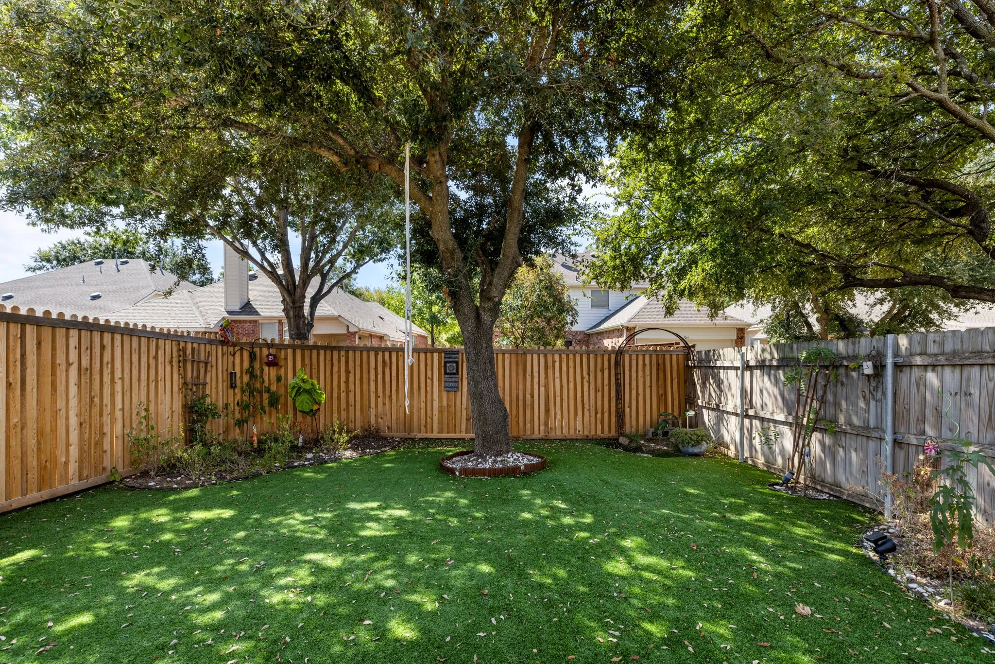 Manicured artificial turf, mature shade tree, natural wood fencing, arched trellis gate