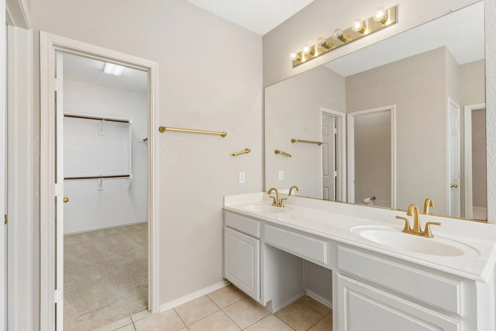 Double vanity with white cabinetry, light-toned countertops, and gold-finish fixtures