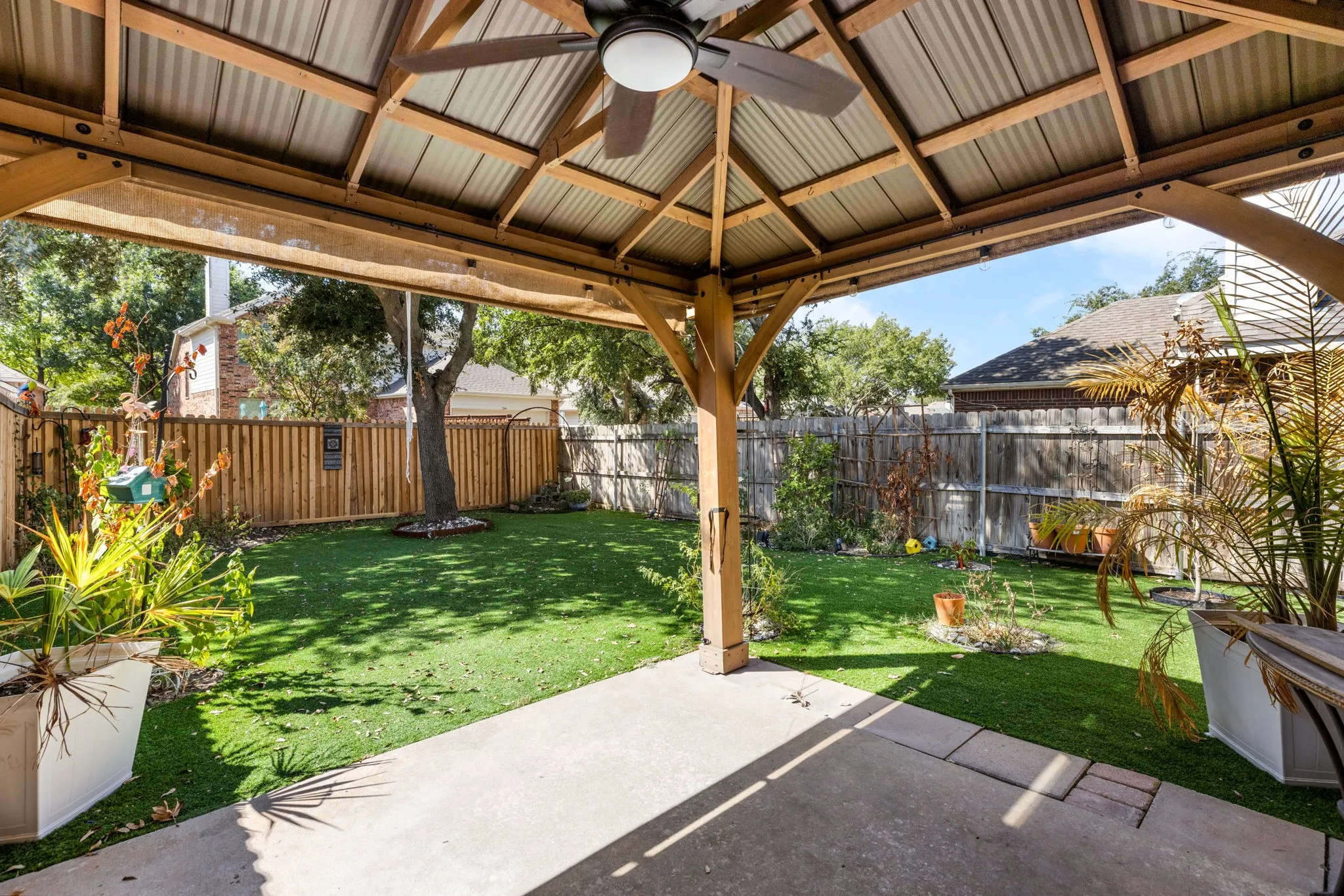 Outdoor patio structure featuring a corrugated metal roof, wood-finish beams, and a ceiling fan