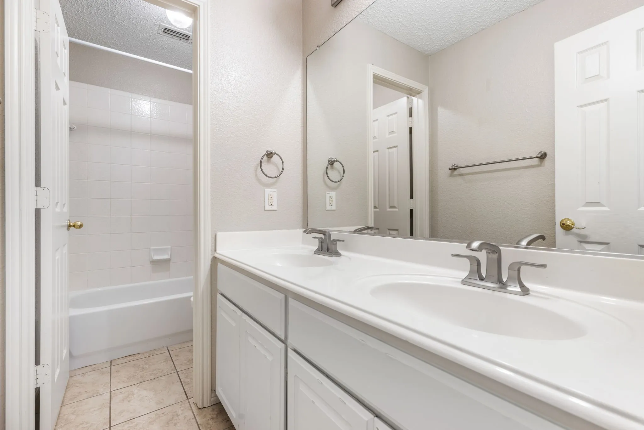 Double vanity with integrated sinks, white cabinetry, chrome fixtures, and a shower-over-tub combination with white tile surround