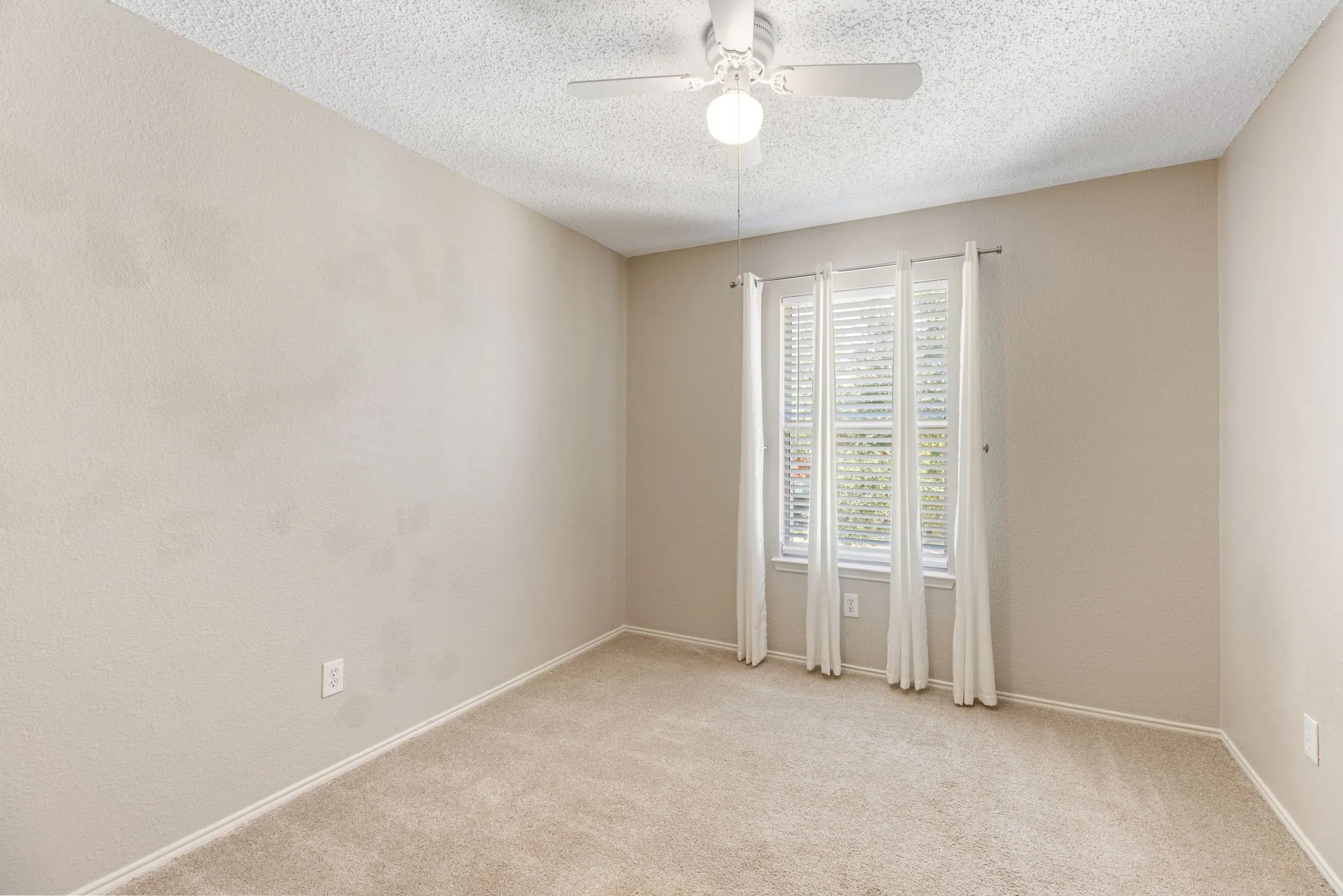 Carpeted room with a ceiling fan light fixture and a multi-pane window with blinds