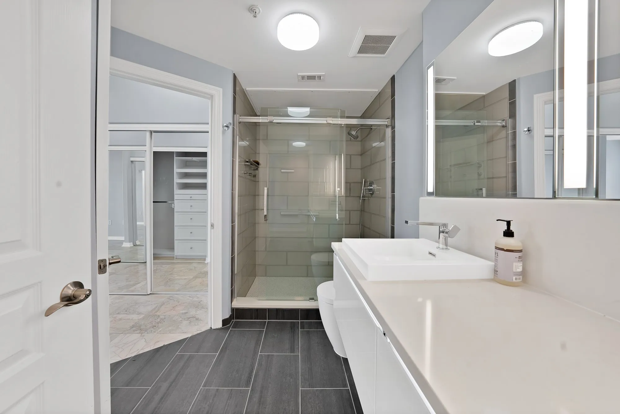 Contemporary bathroom with a glass-enclosed shower, integrated sink vanity, light-toned countertop, and dark rectangular floor tiles