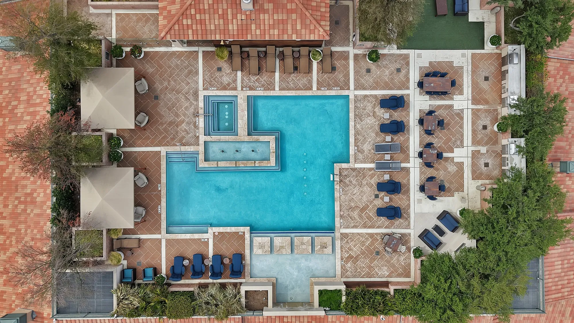 Expansive outdoor common area featuring a multi-level swimming pool, integrated spa, tiled patio, and lush perimeter landscaping