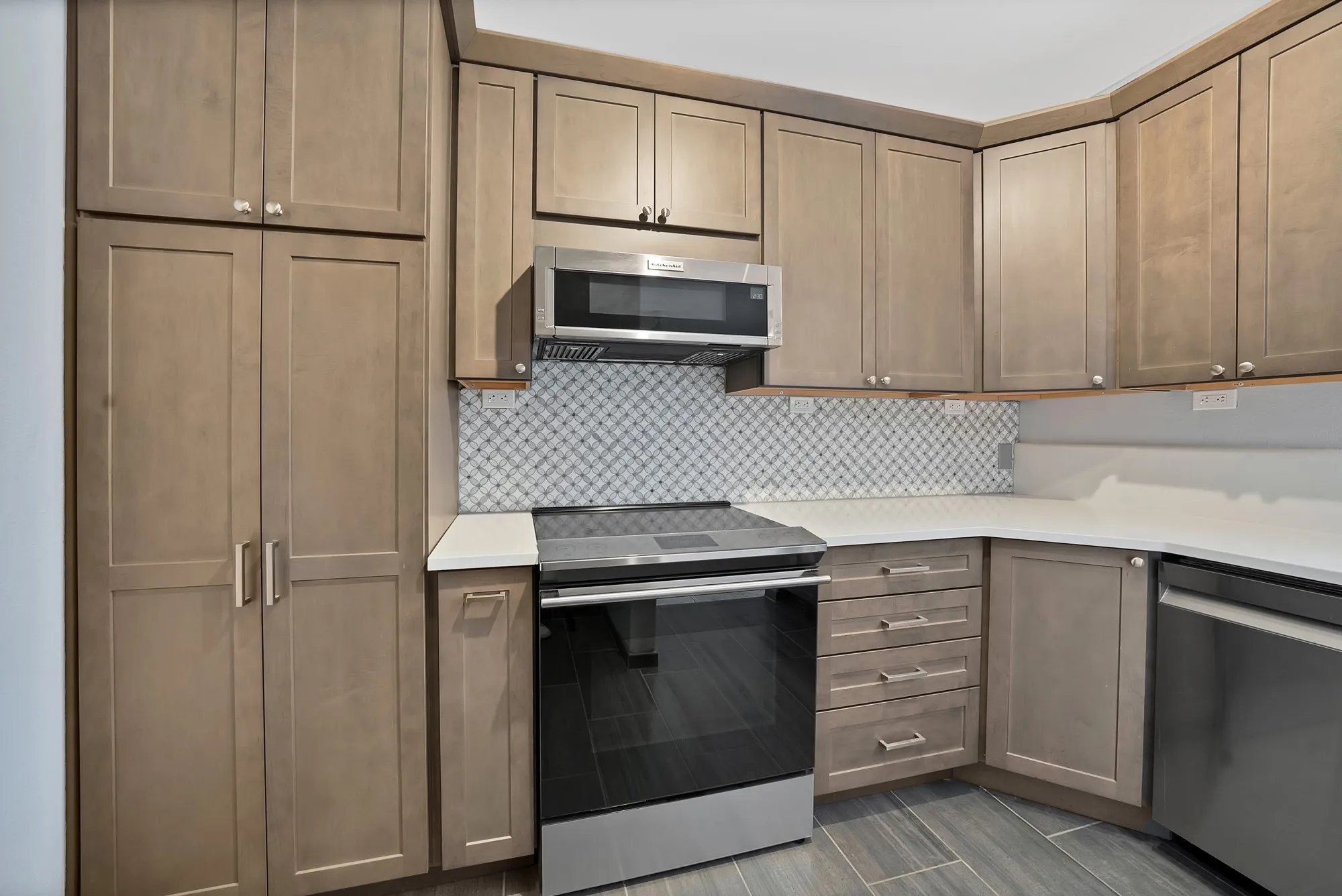 Kitchen featuring wood-finish cabinetry, stainless steel appliances, patterned tile backsplash, white countertops, and tile flooring