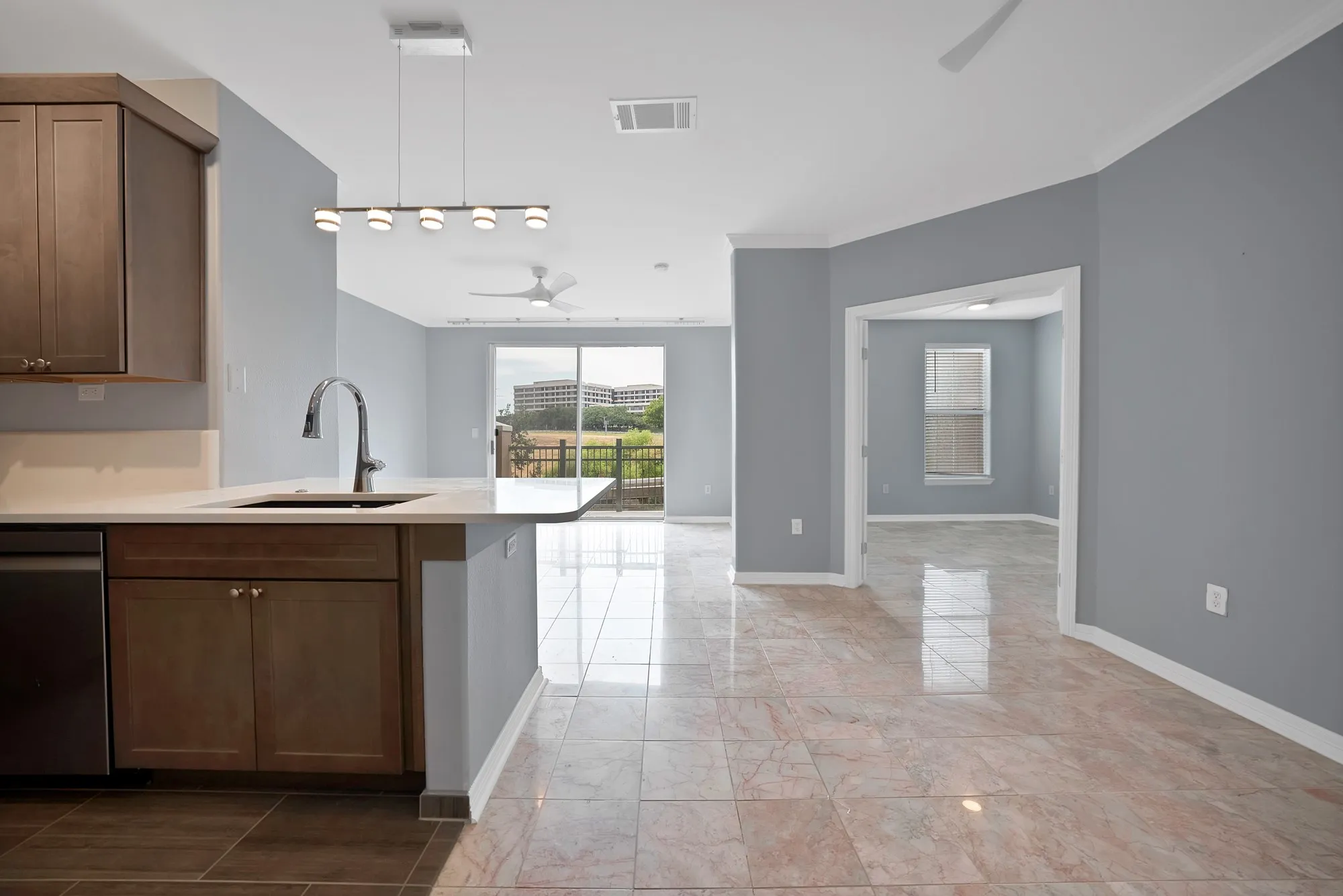 Kitchen island with a built-in sink and gooseneck faucet, stainless steel dishwasher, wood-finish cabinetry, and light-toned countertop