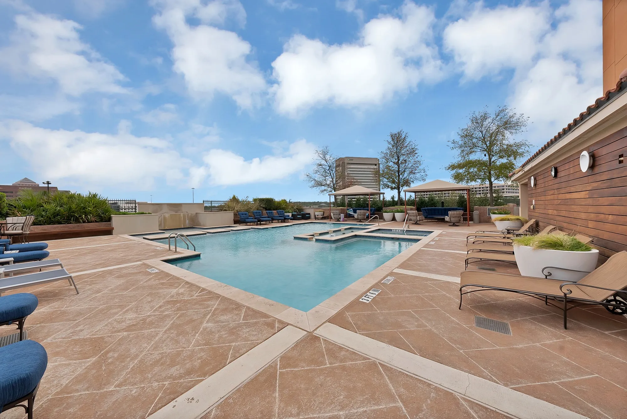 Rooftop pool deck with a geometric pool, two integrated spas, stamped concrete surfacing, and a wood-slat exterior wall