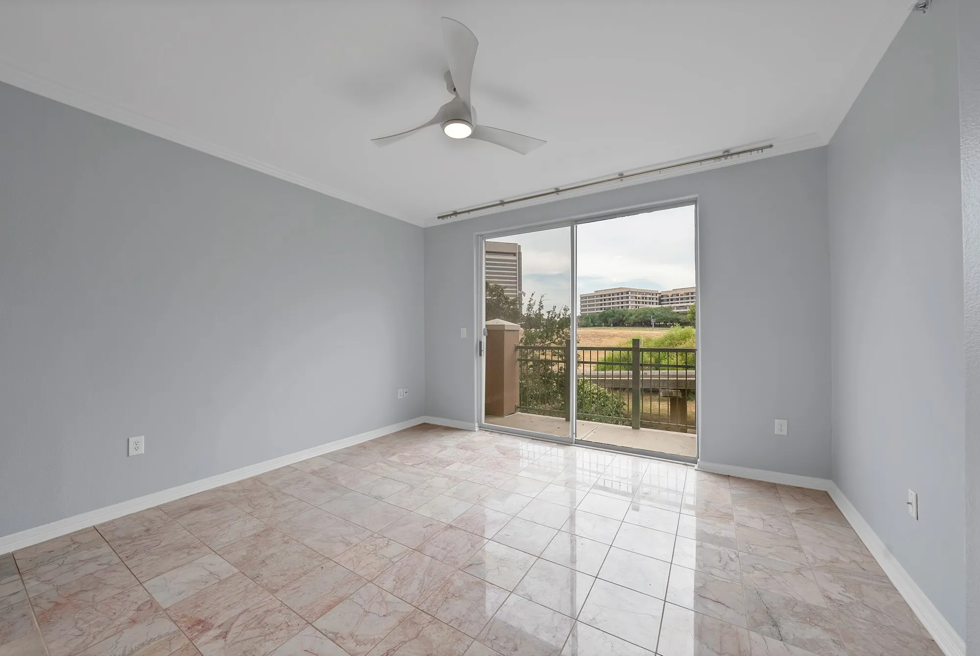 Spacious room featuring tile flooring, light gray walls, a ceiling fan with integrated lighting, and a sliding glass door leading to a balcony with metal railings