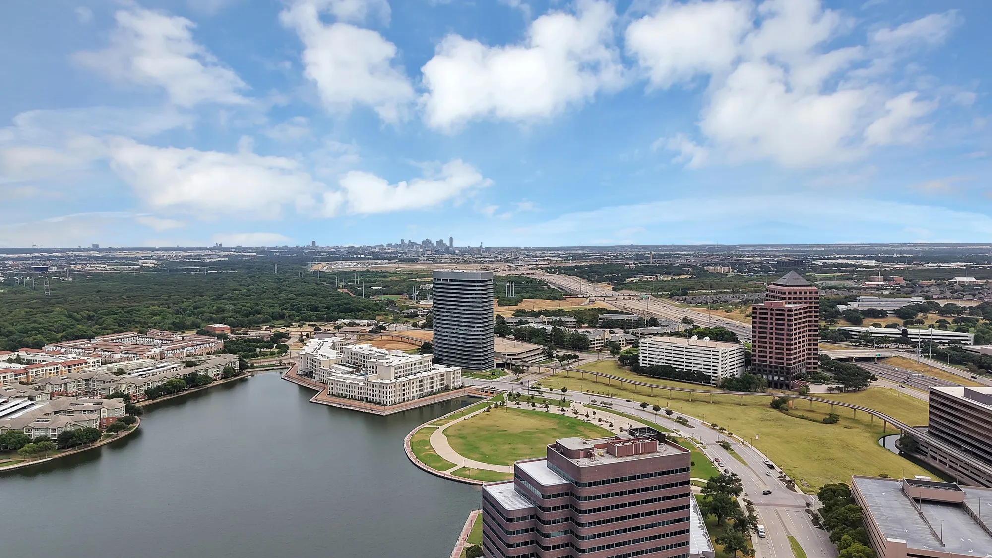 Expansive urban landscape featuring a large body of water, green park spaces, and multiple high-rise buildings