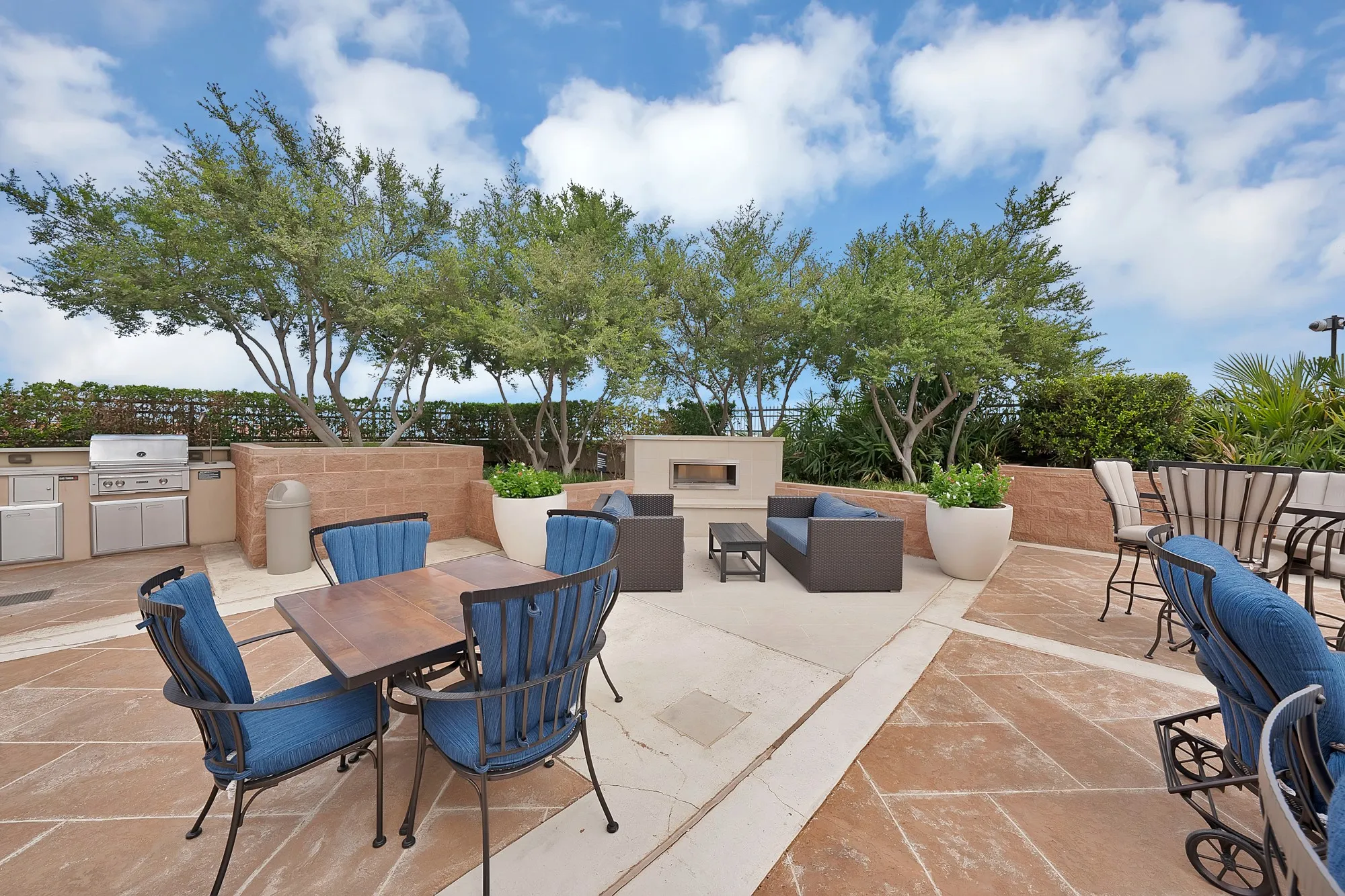 Expansive outdoor patio with stone paving, built-in outdoor kitchen, integrated fireplace, and mature trees