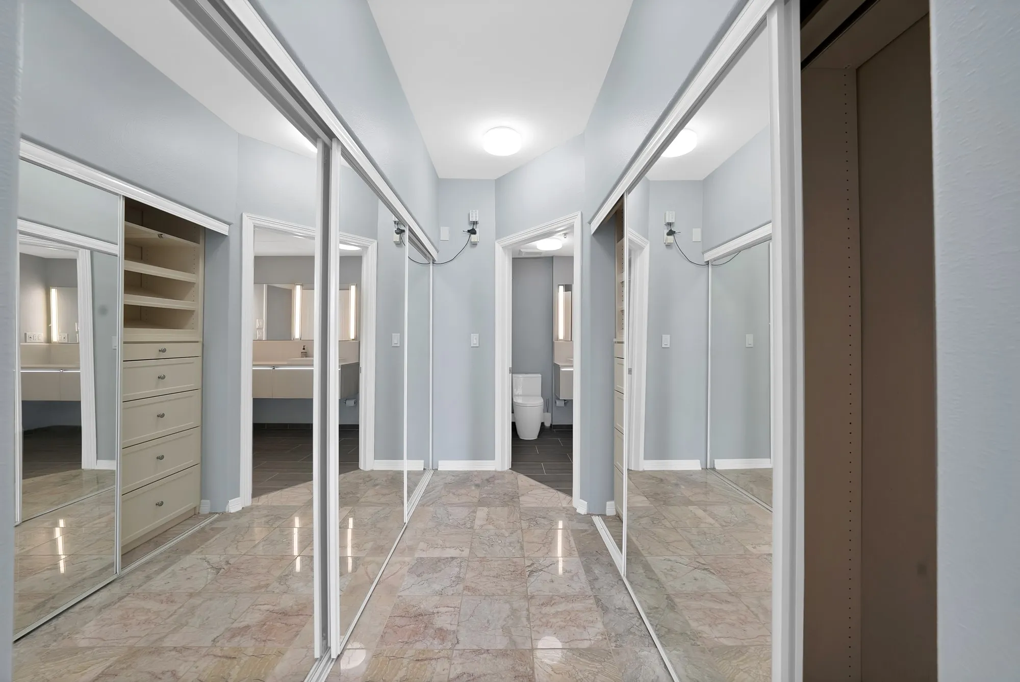 Mirrored sliding closet doors, built-in closet organization with drawers and shelving, recessed lighting, and stone flooring
